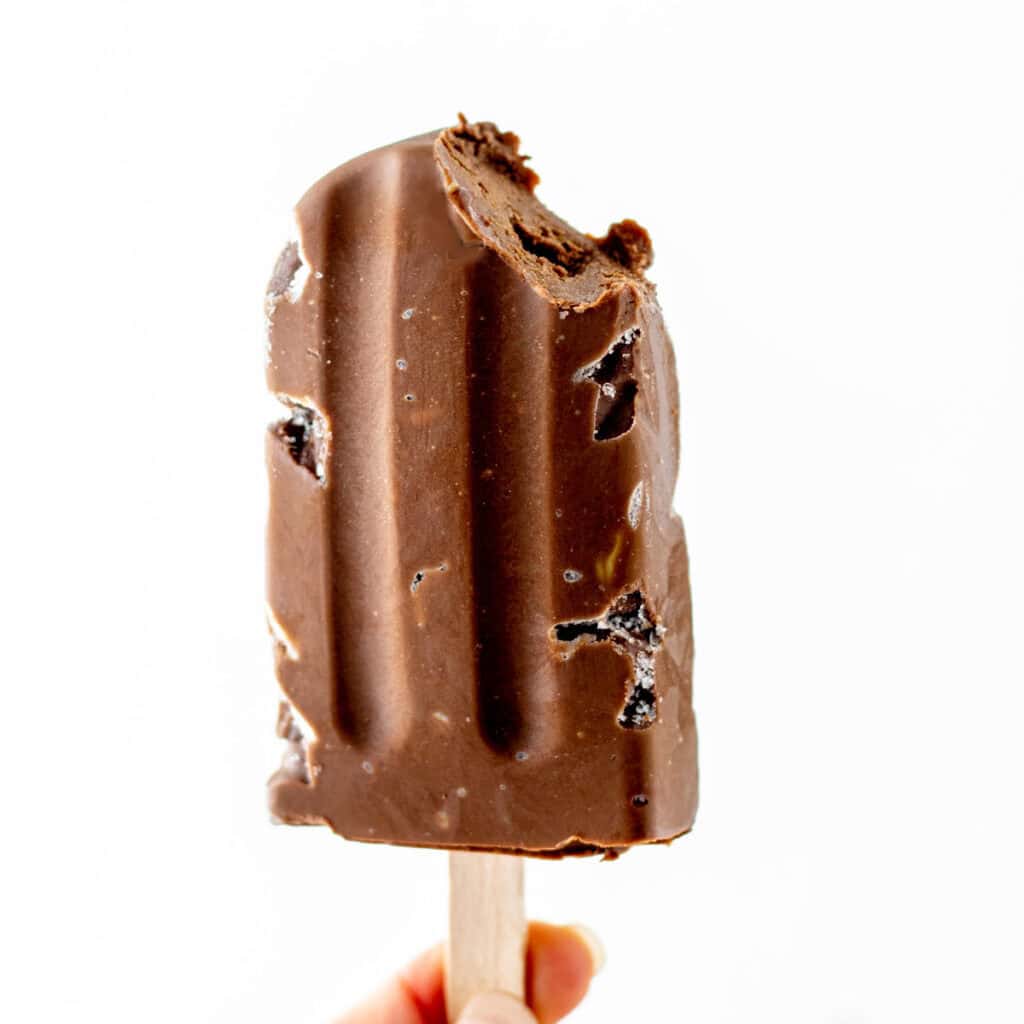A hand holding a chocolate avocado popsicle with a bite taken out of it.