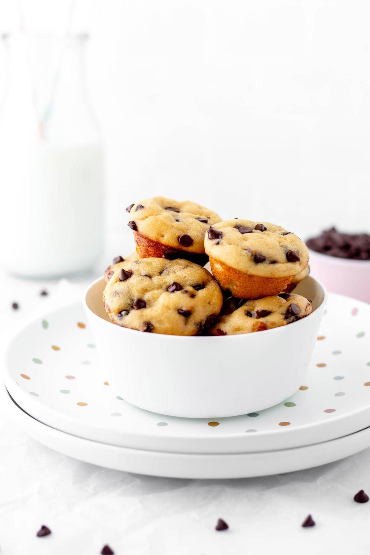 Mini chocolate chip muffins stacked on top of one another in a white bowl on a plate.