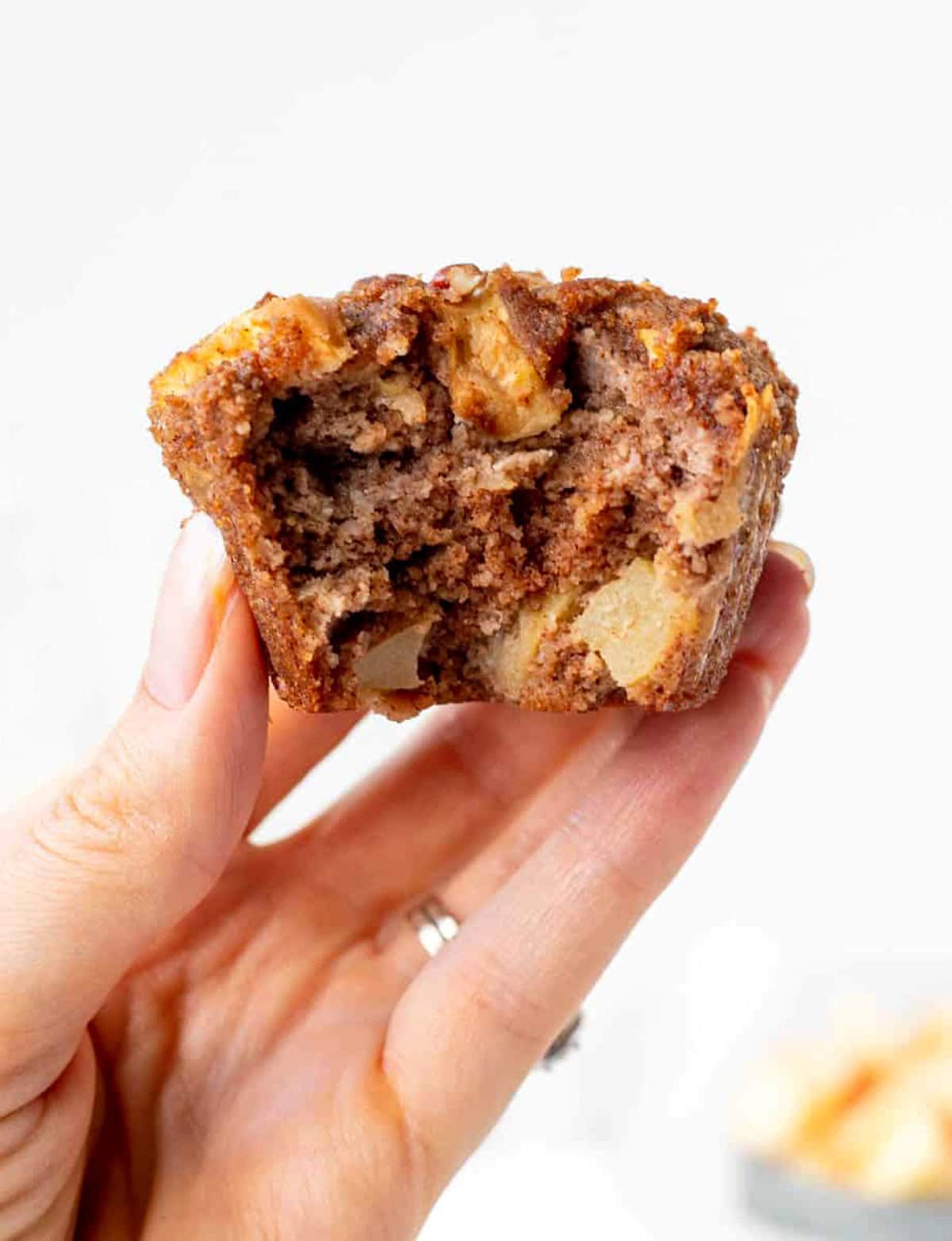 A hand holding a gluten-free apple muffin with a bite taken out of it.