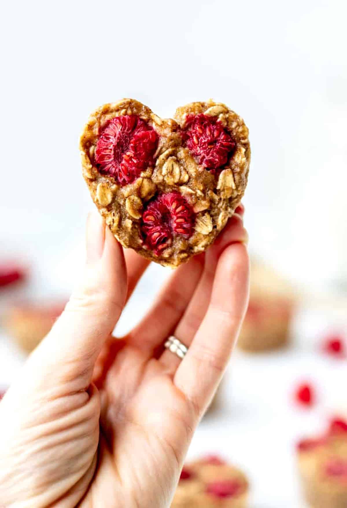 A hand holding up a raspberry banana oatmeal muffin.