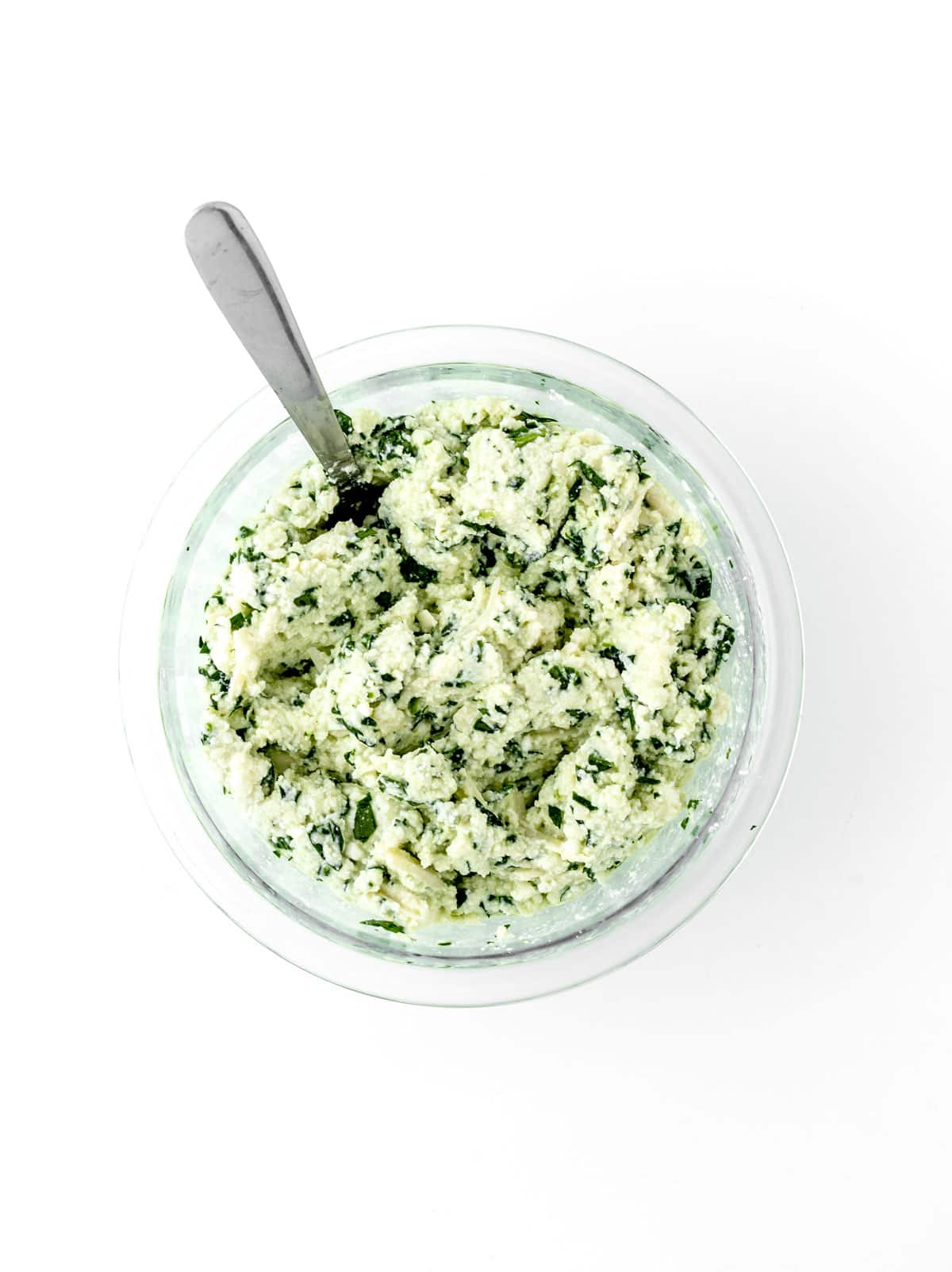 The ricotta mixture in a clear glass bowl with a spoon.