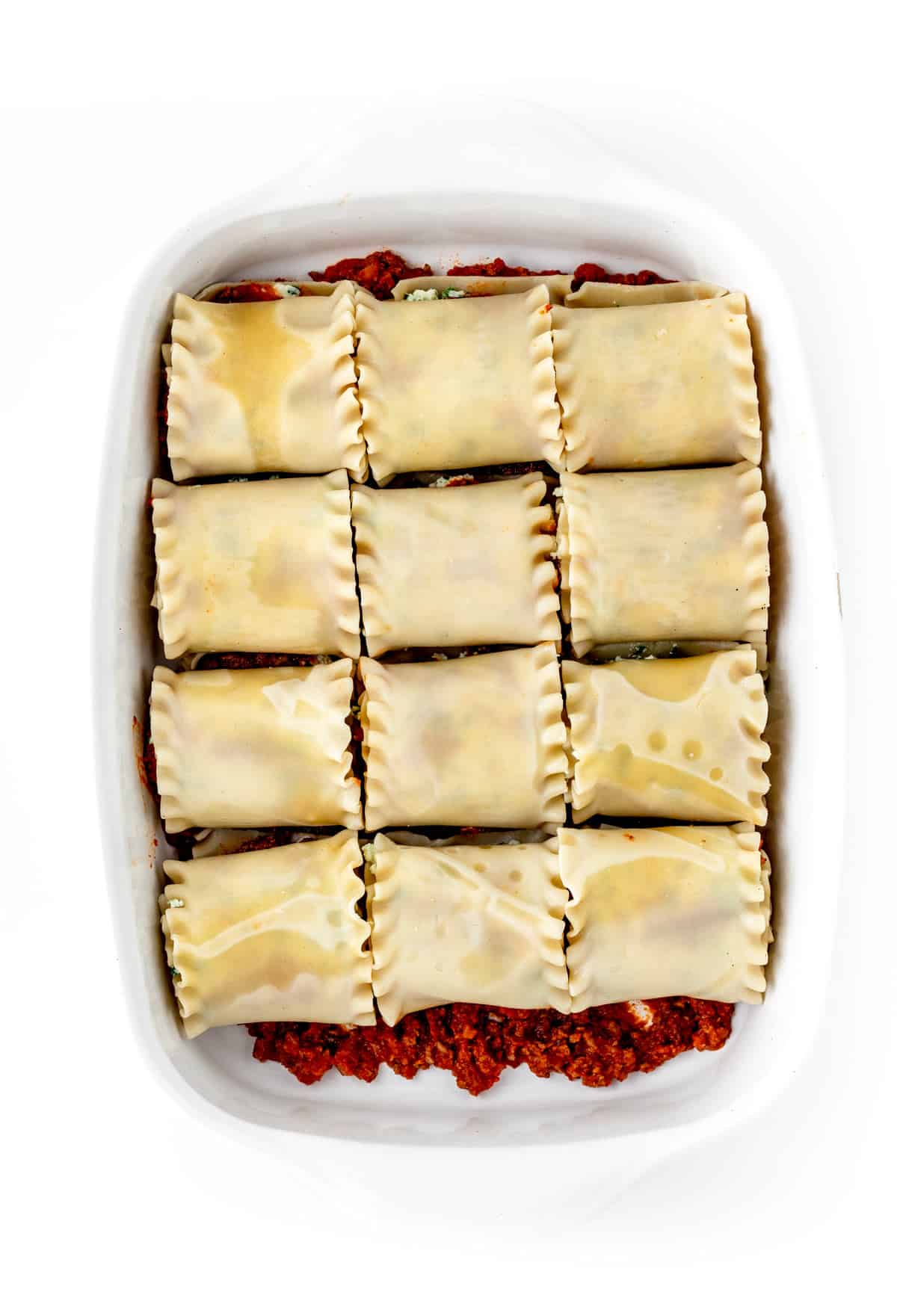 The lasagna noodles formed into roll ups in a baking dish, prior to cooking.
