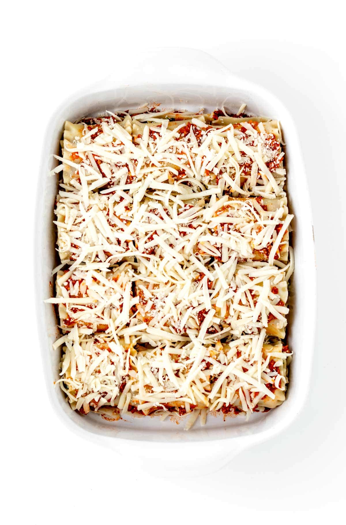 Hidden veggie lasagna roll ups covered in cheese in a baking dish, prior to baking.