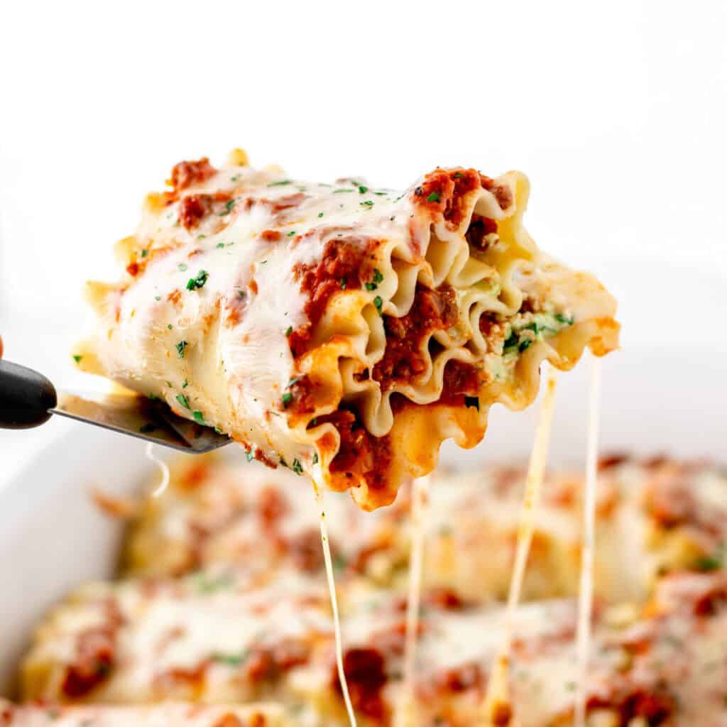 A spatula holding up a lasagna roll up with cheese pulls.
