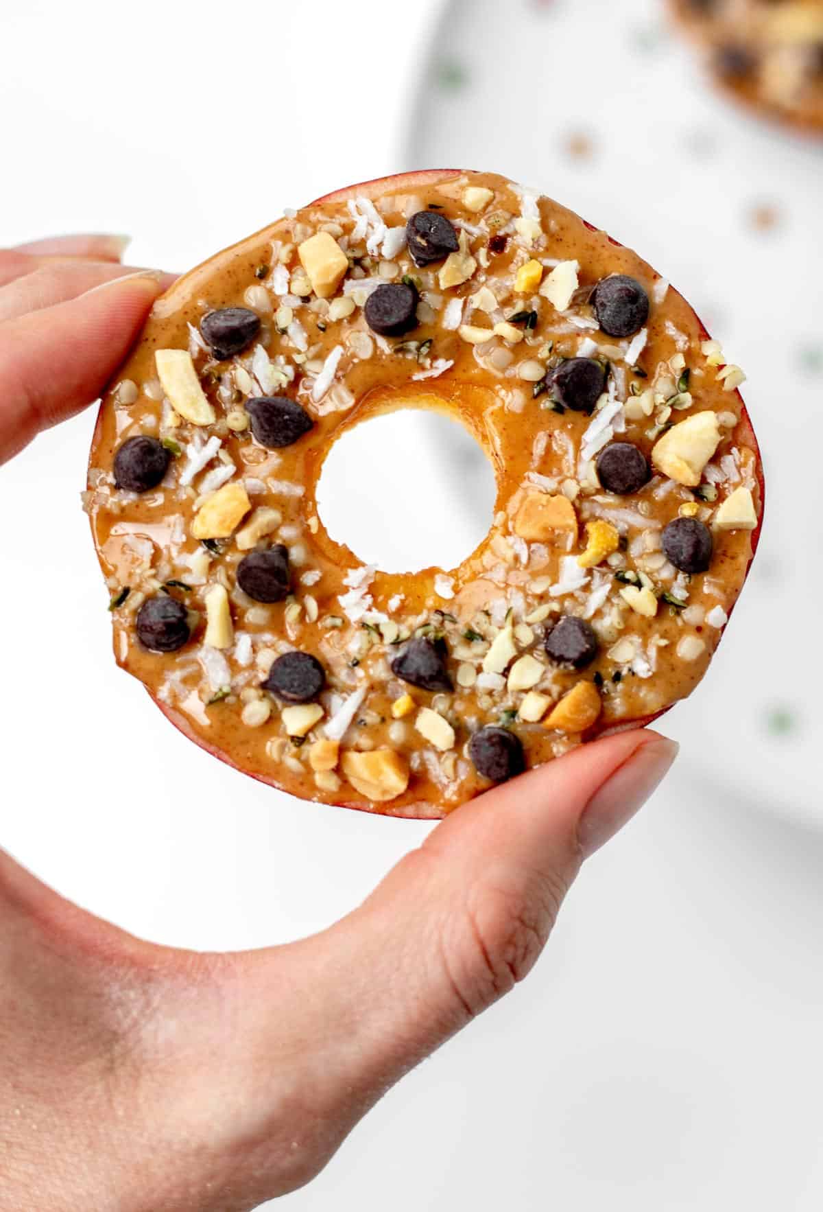 A closeup of an apple slice cookie being held in between someone's thumb and forefinger.