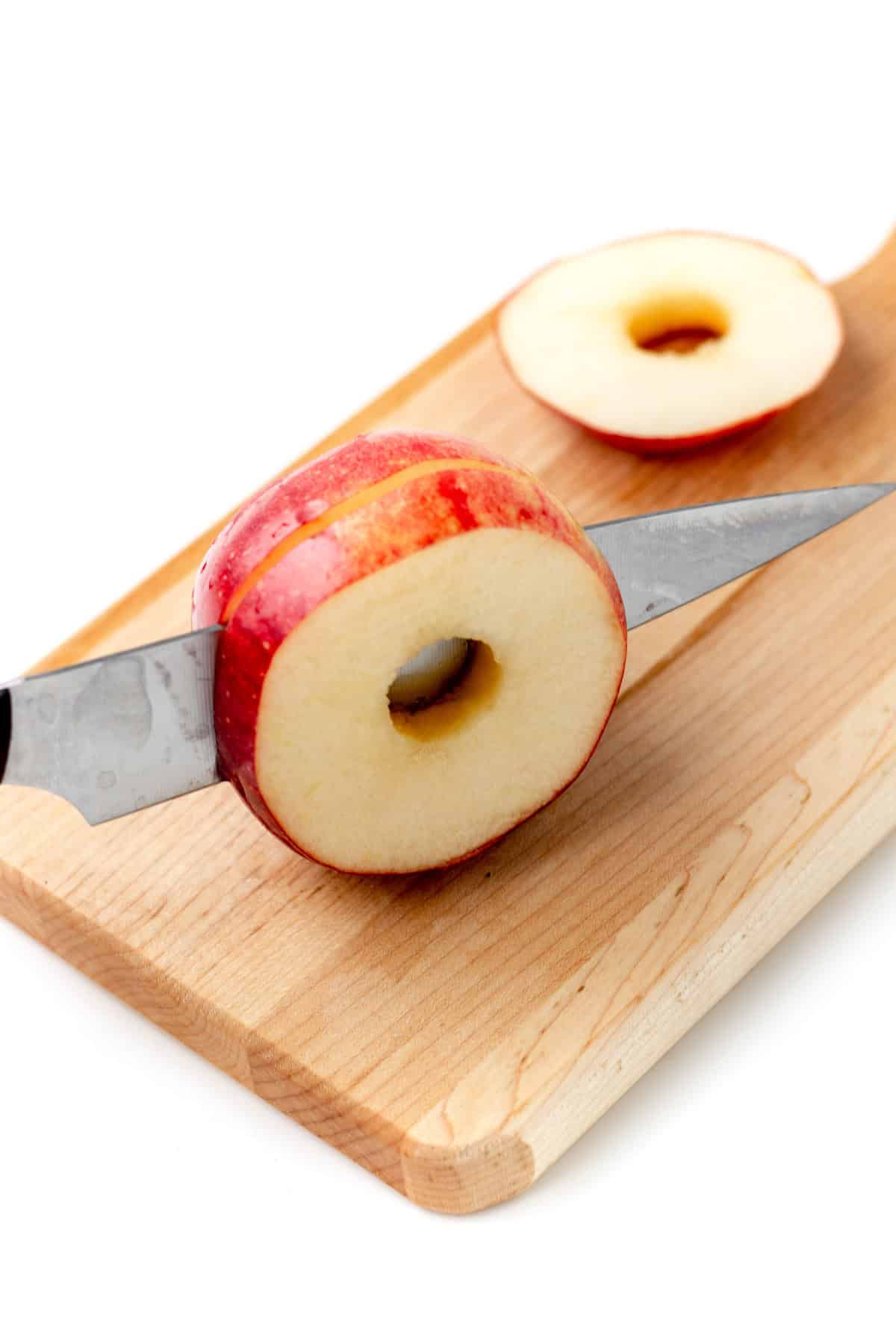 Using a sharp knife to cut slices out of a cored apple on a wooden cutting board.