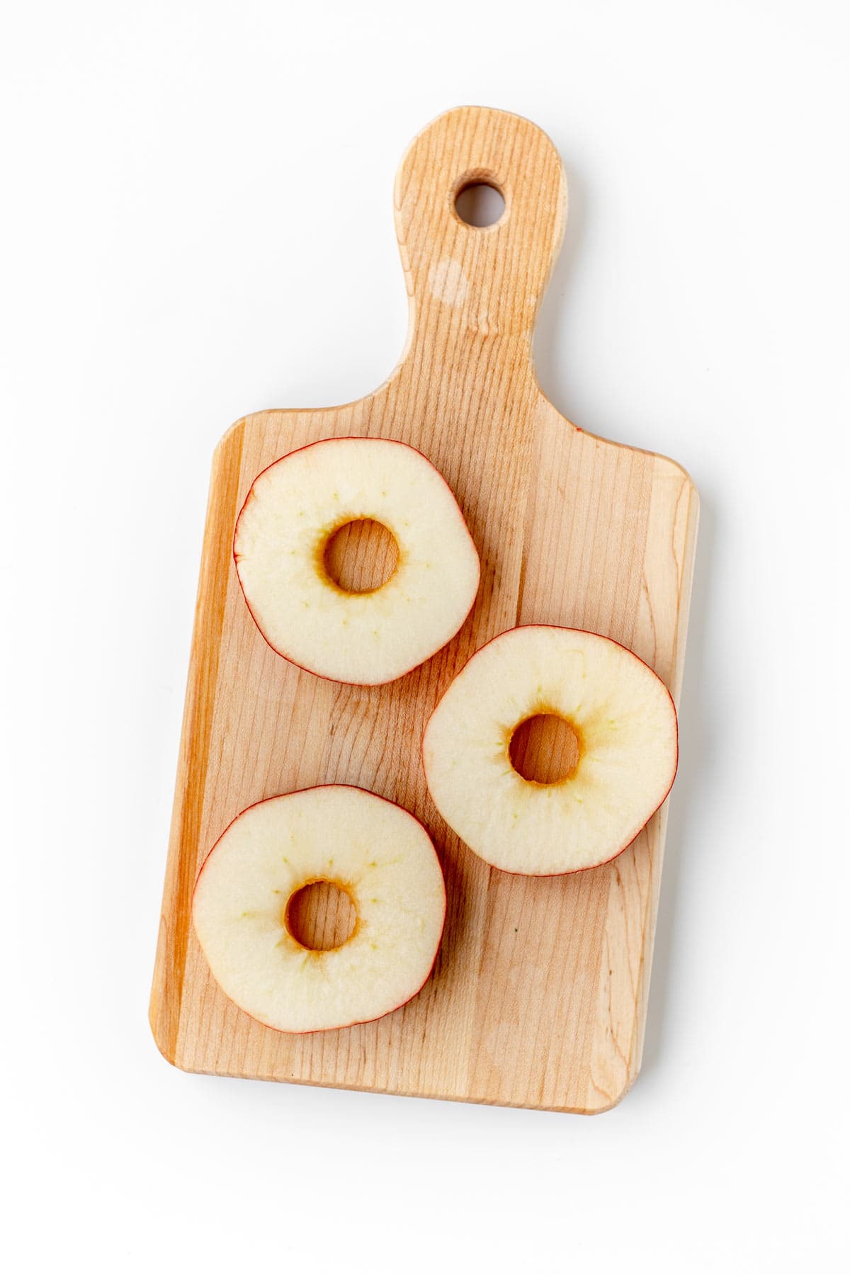 Three cored apple slices on a wooden cutting board.