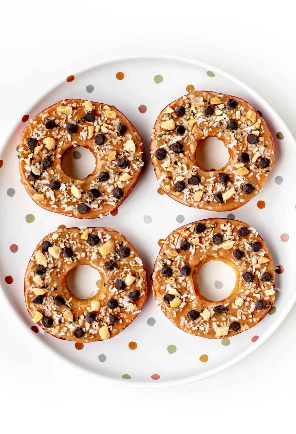 Apple slice cookies topped with peanut butter, shredded coconut and mini chocolate chips on a polka dot plate.