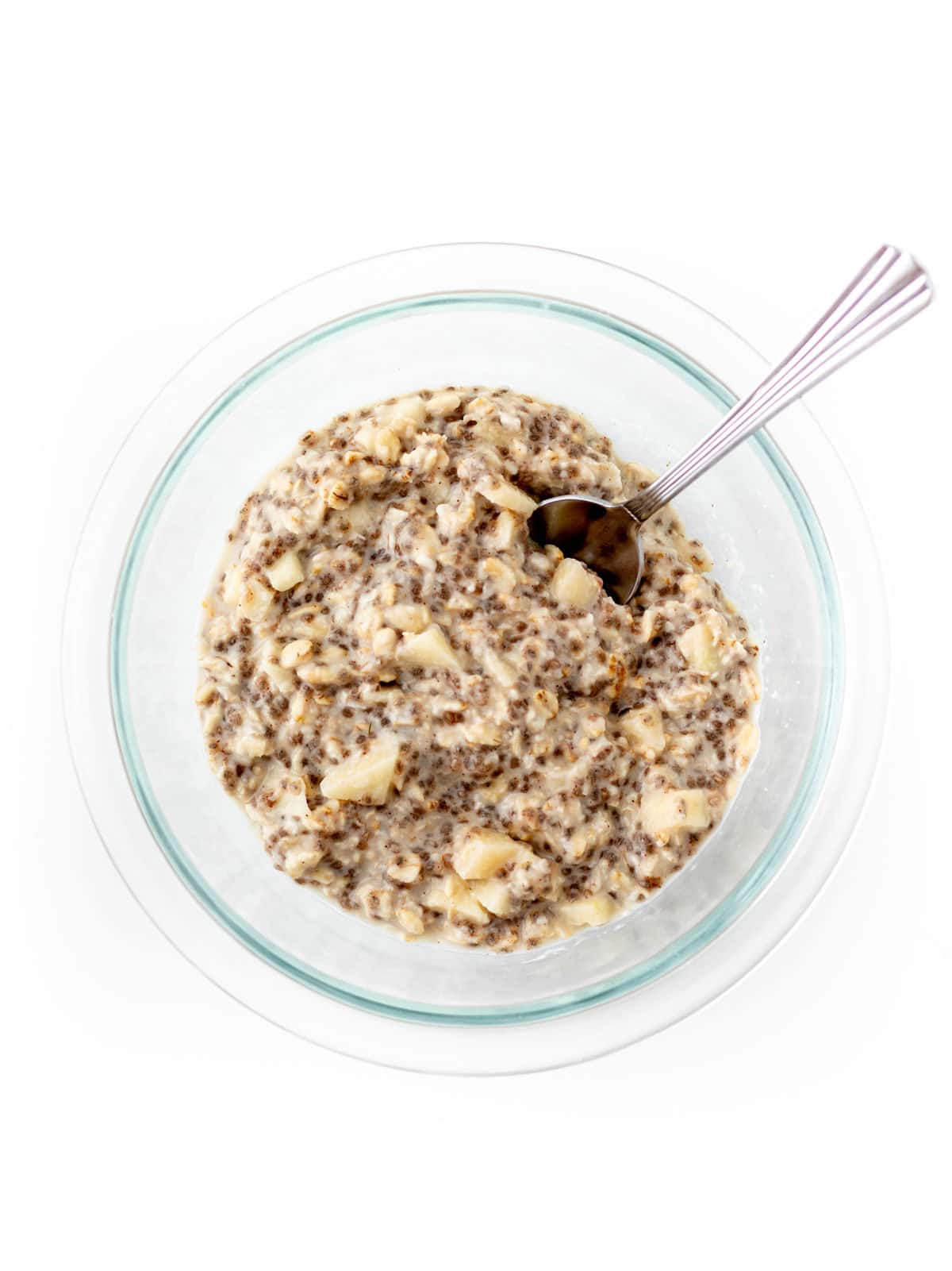 Mixing the applesauce overnight oats in a glass bowl with a spoon.