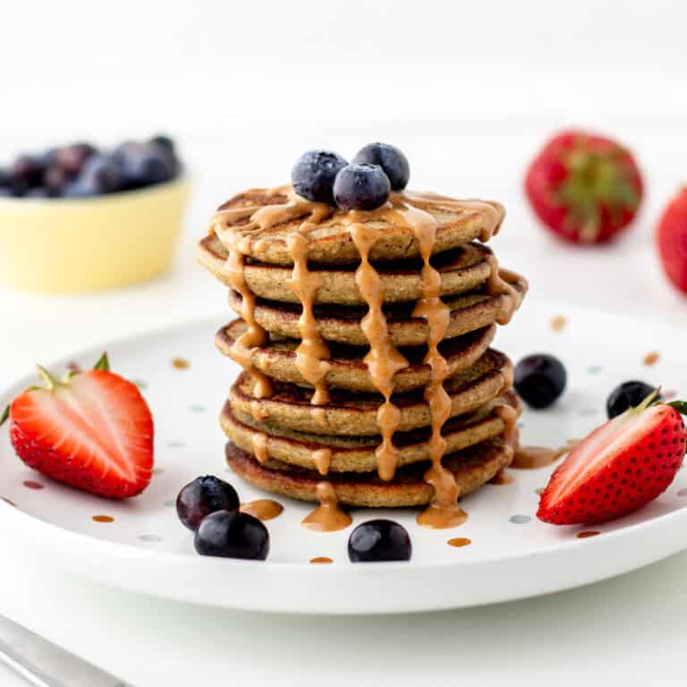 A stack of zucchini oatmeal pancakes topped with nut butter and berries.