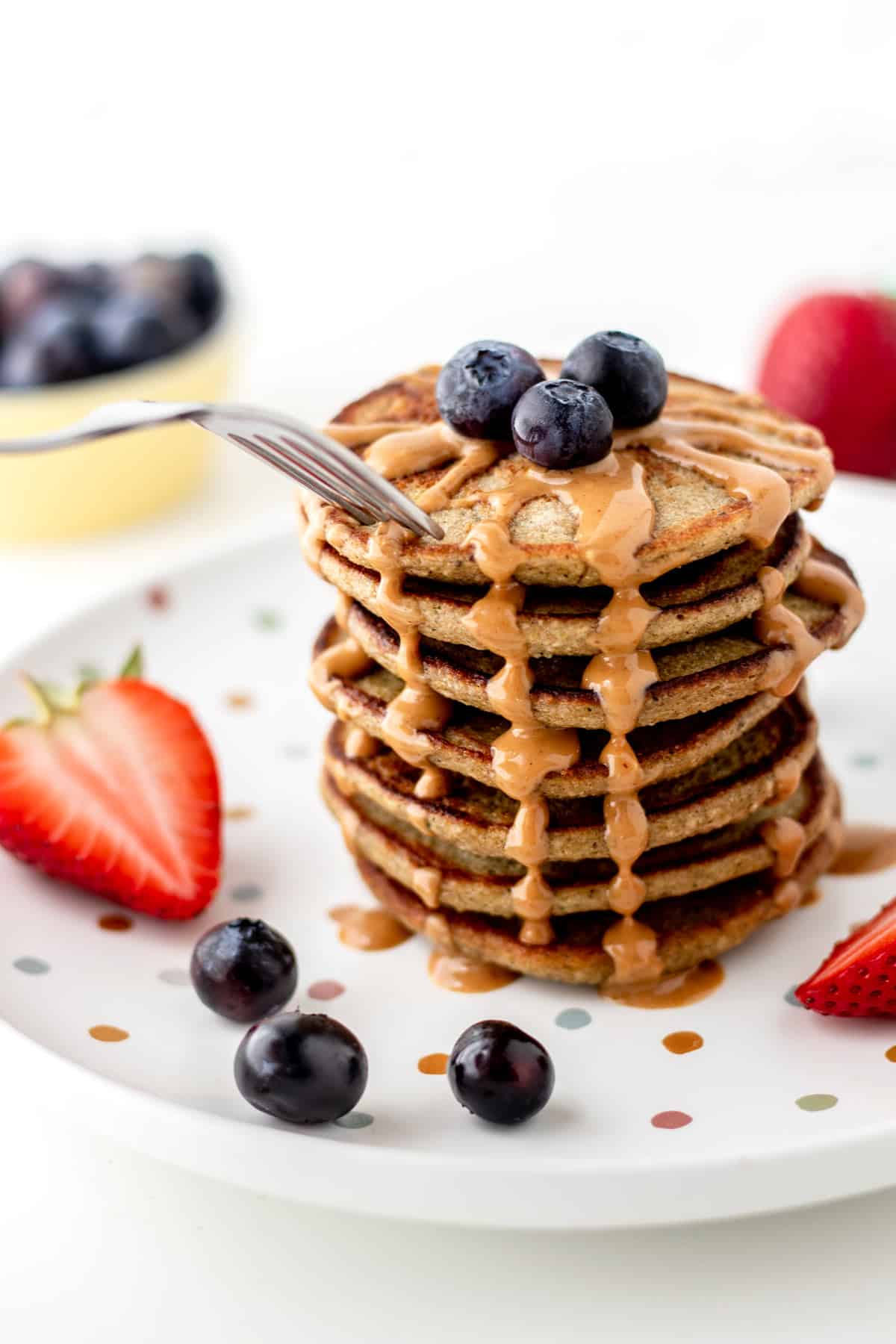 A stack of banana zucchini pancakes, topped with blueberries and peanut butter.