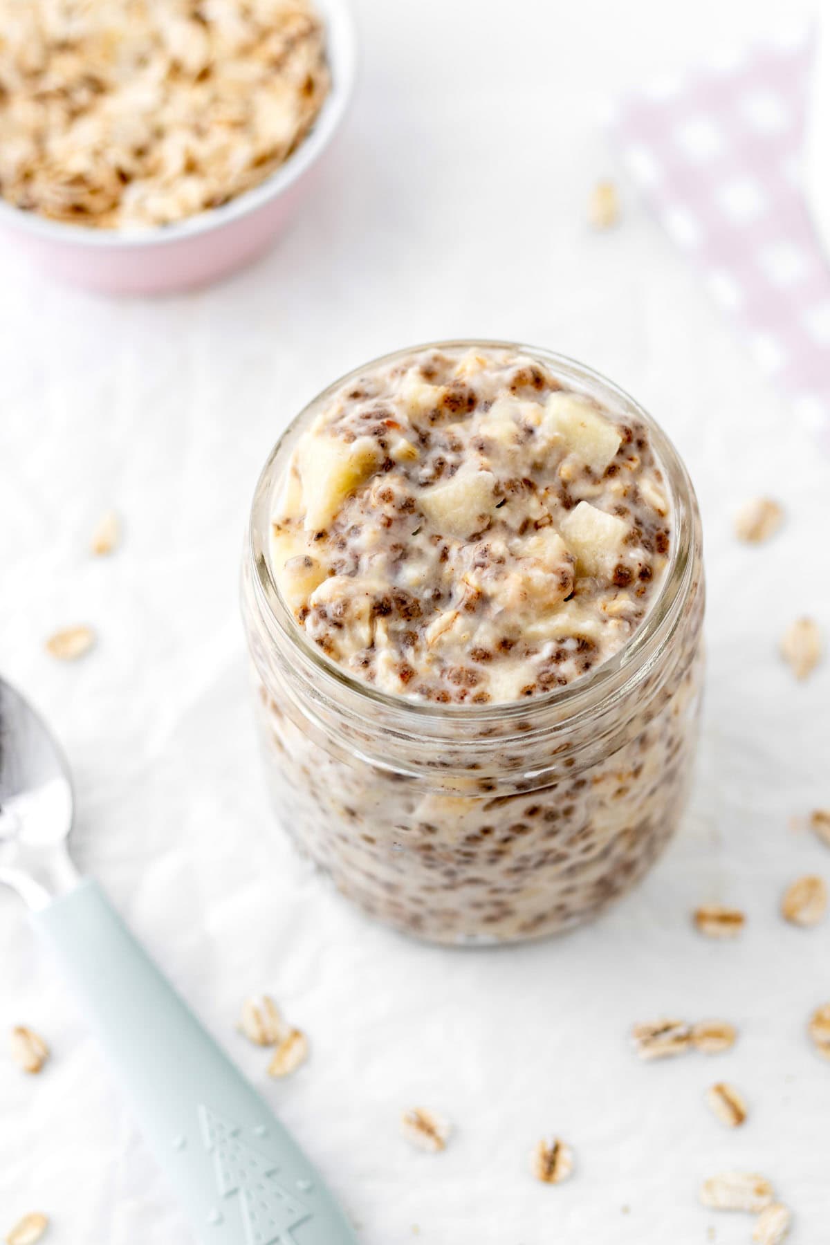 Overnight oats with applesauce in a glass jar on a counter next to a spoon.