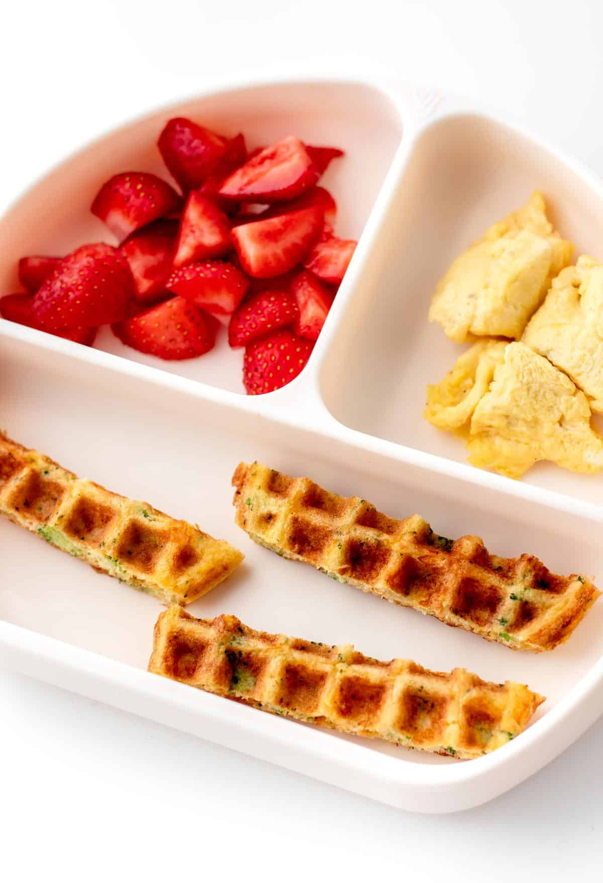 A pink divided plate with strips of broccoli cheese waffle, mixed berries and eggs.