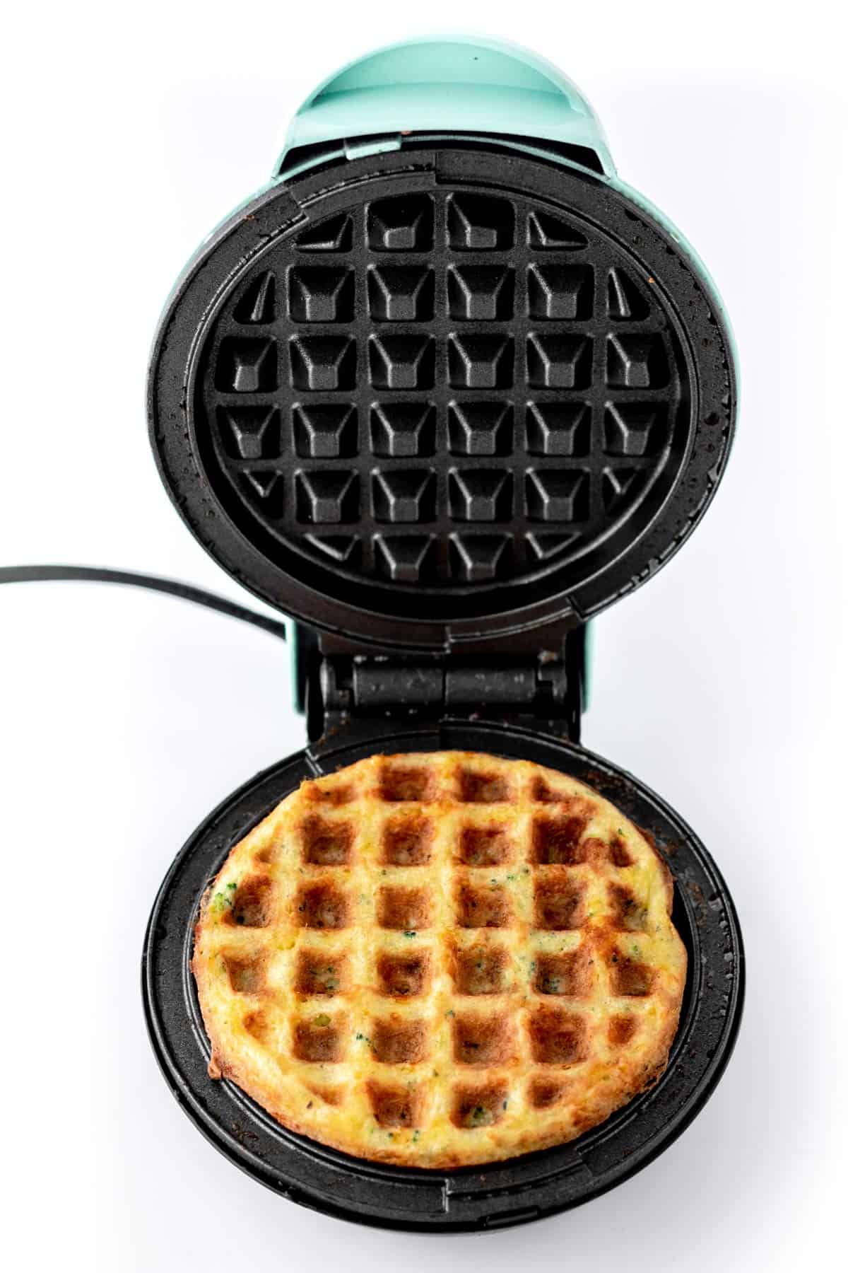 A broccoli cheese waffle in a waffle iron.