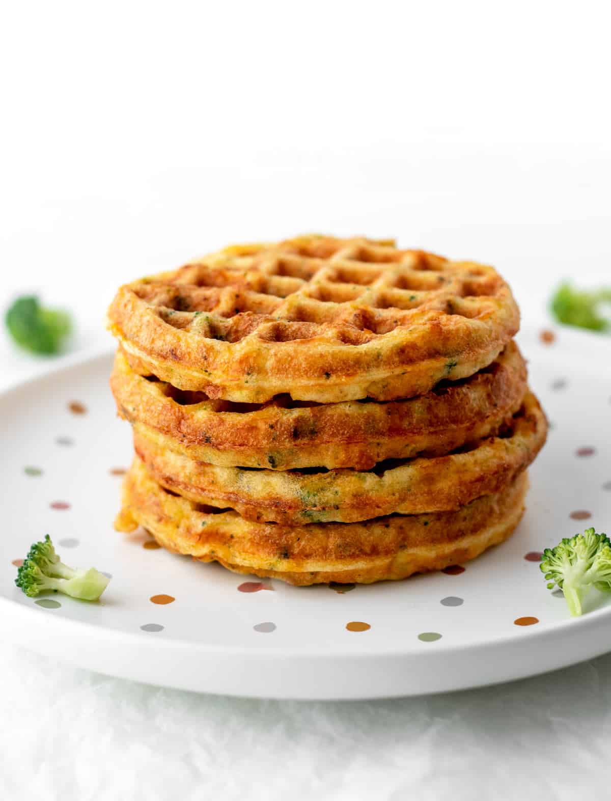 Four broccoli cheese waffles stacked on top of each other on a polka dot plate.