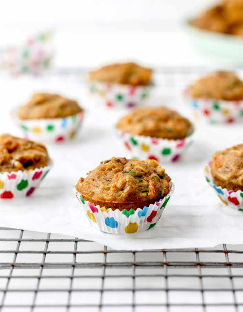 Carrot zucchini and banana muffins spread out on a cooling rack.