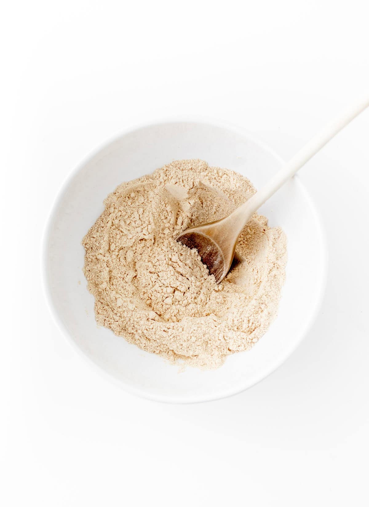 A bowl of flour with a wooden spoon in it.