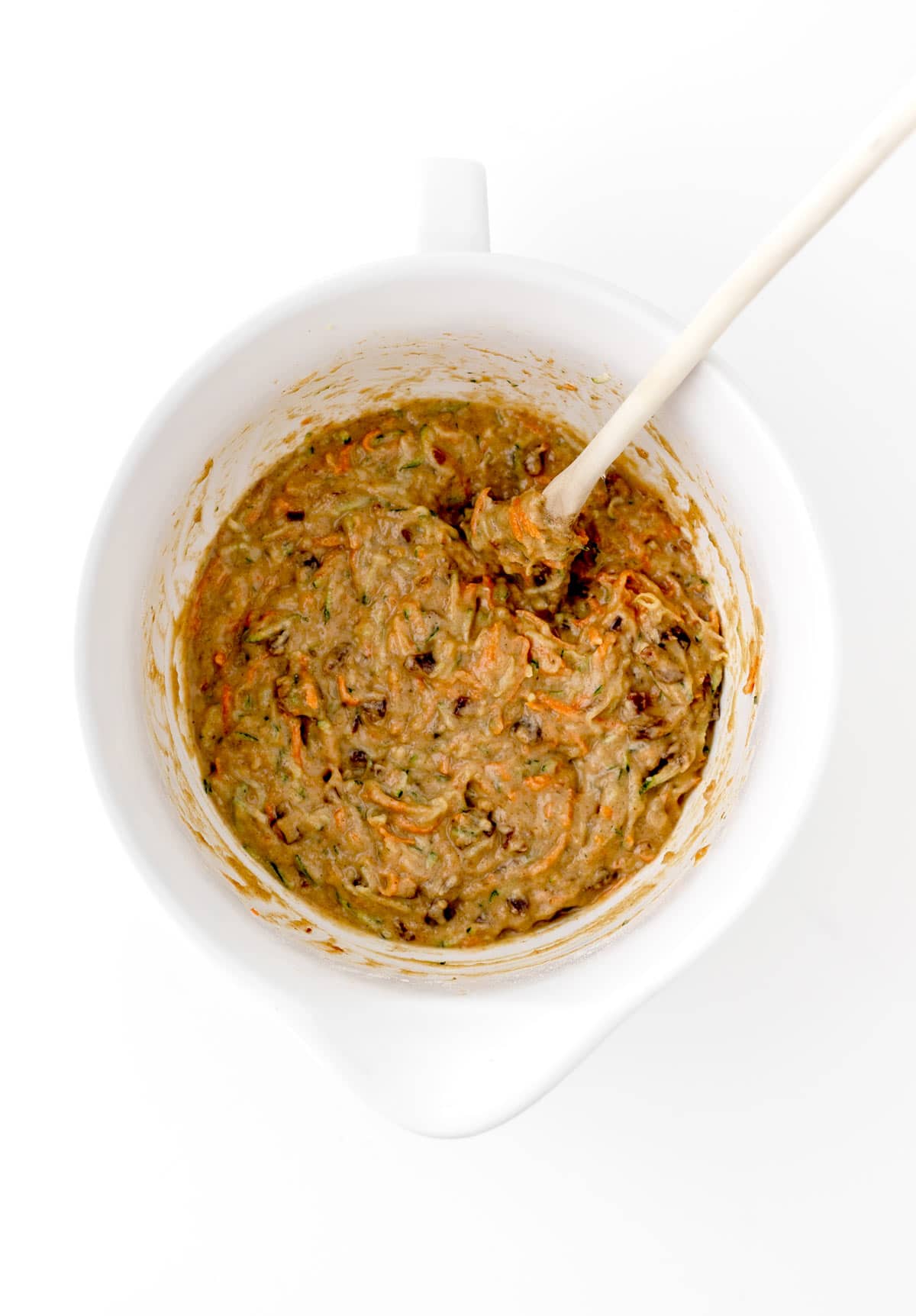 Adding the grated carrots and zucchini to the bowl with the muffin batter, and stirring with a spoon.