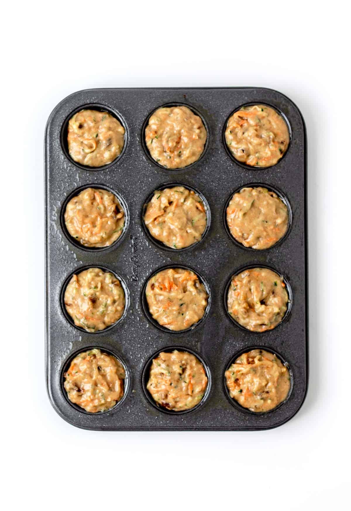 Carrot zucchini muffin batter in a muffin pan prior to baking.