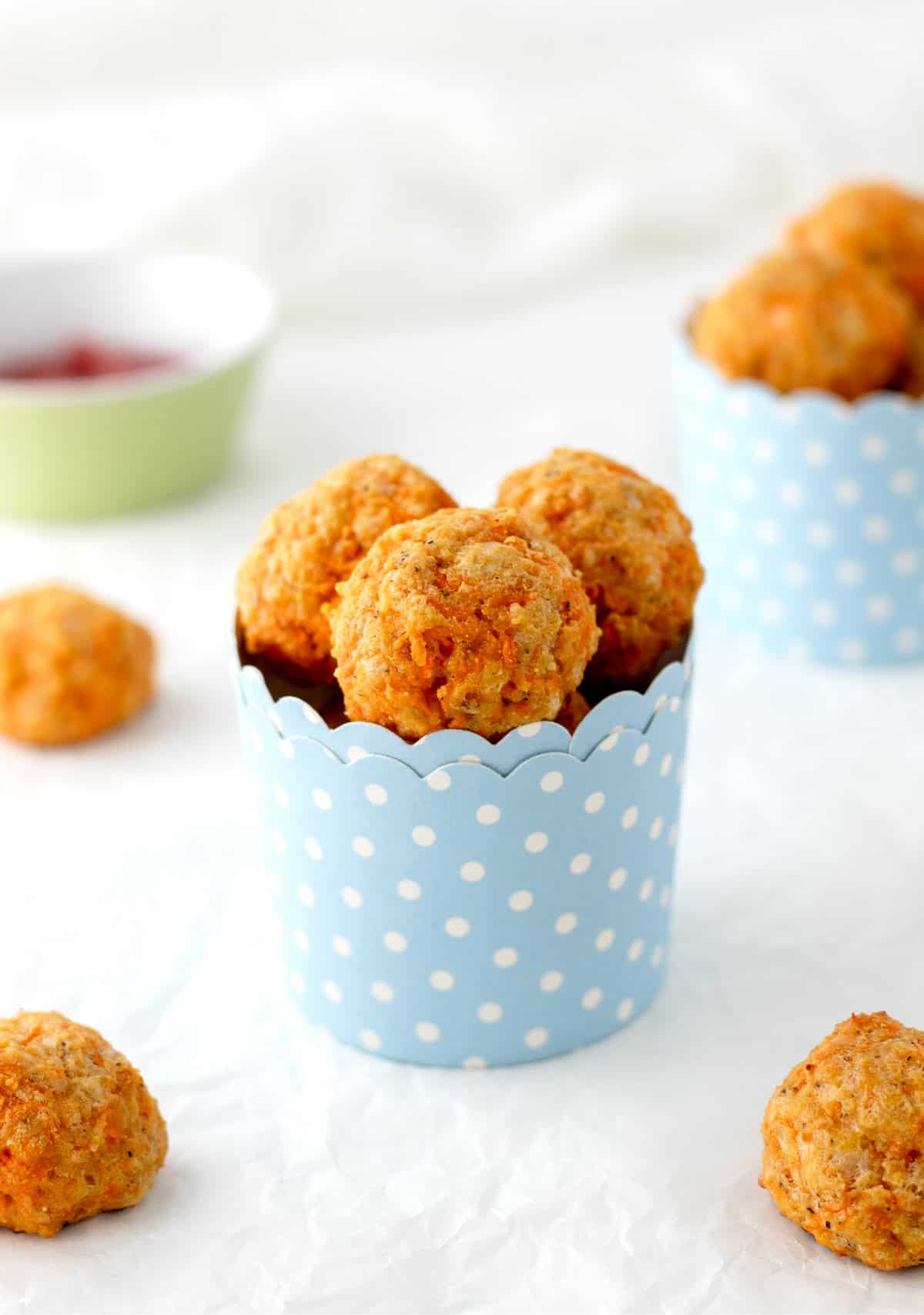 Cheesy carrot balls in a blue and white polka dot cup on a table.