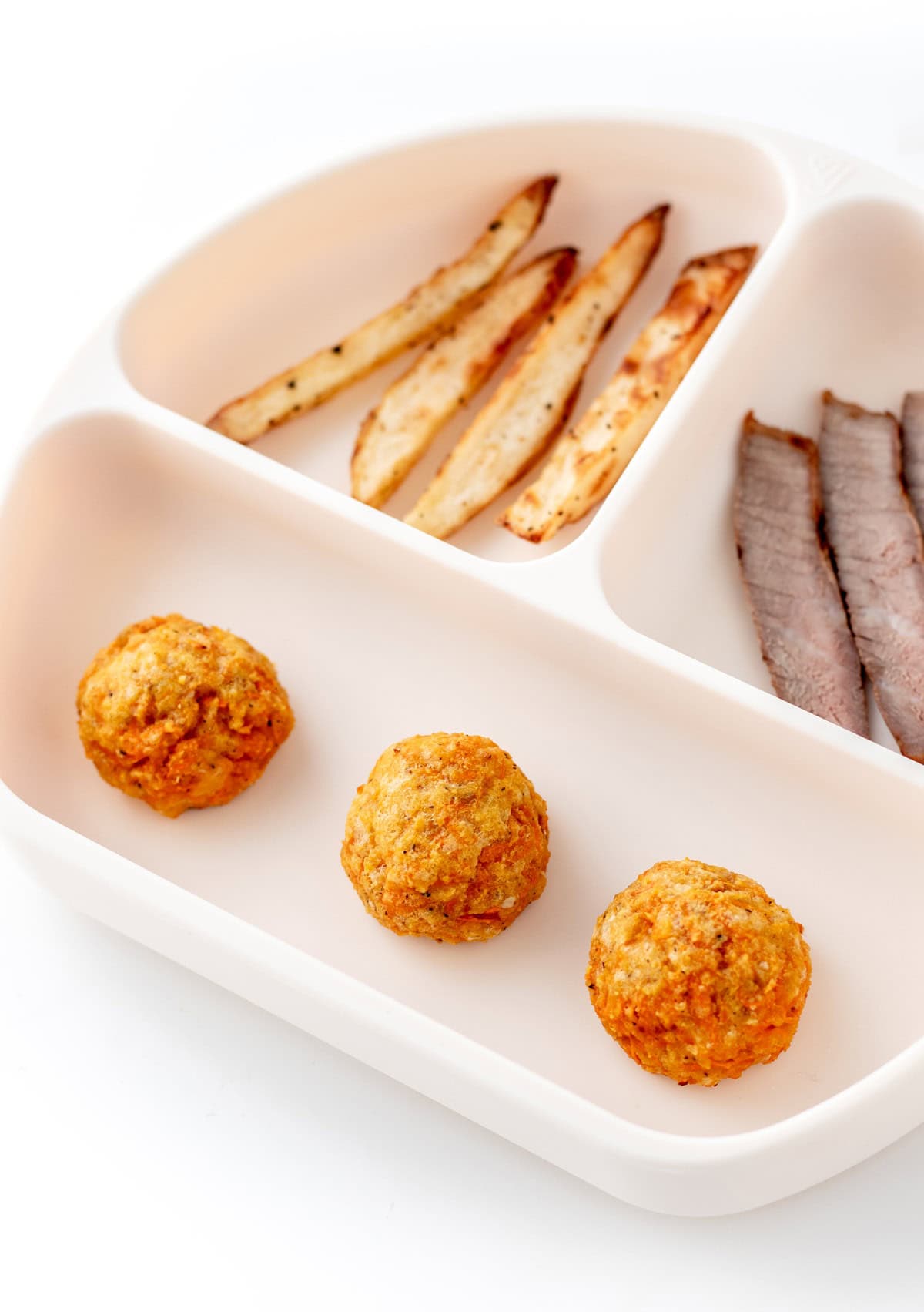 3 cheesy carrot bites on a divided plate with potatoes and sliced meat.