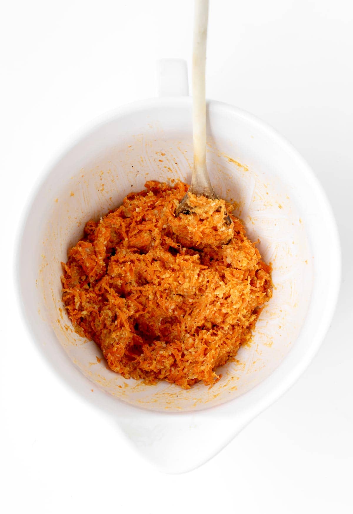 Mixing ingredients for the cheesy carrot bites in a bowl with a spoon.