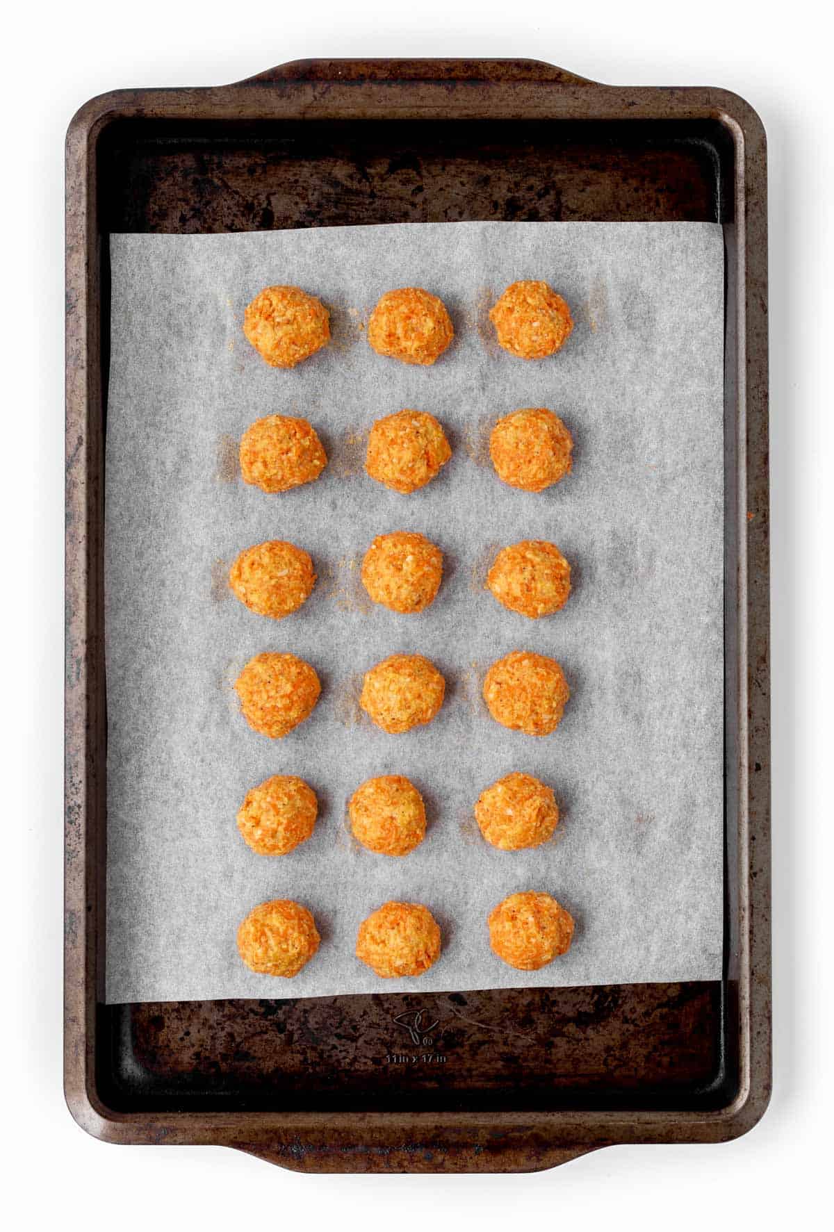 The cheesy carrot bite mixture on a baking sheet lined with parchment paper prior to baking.