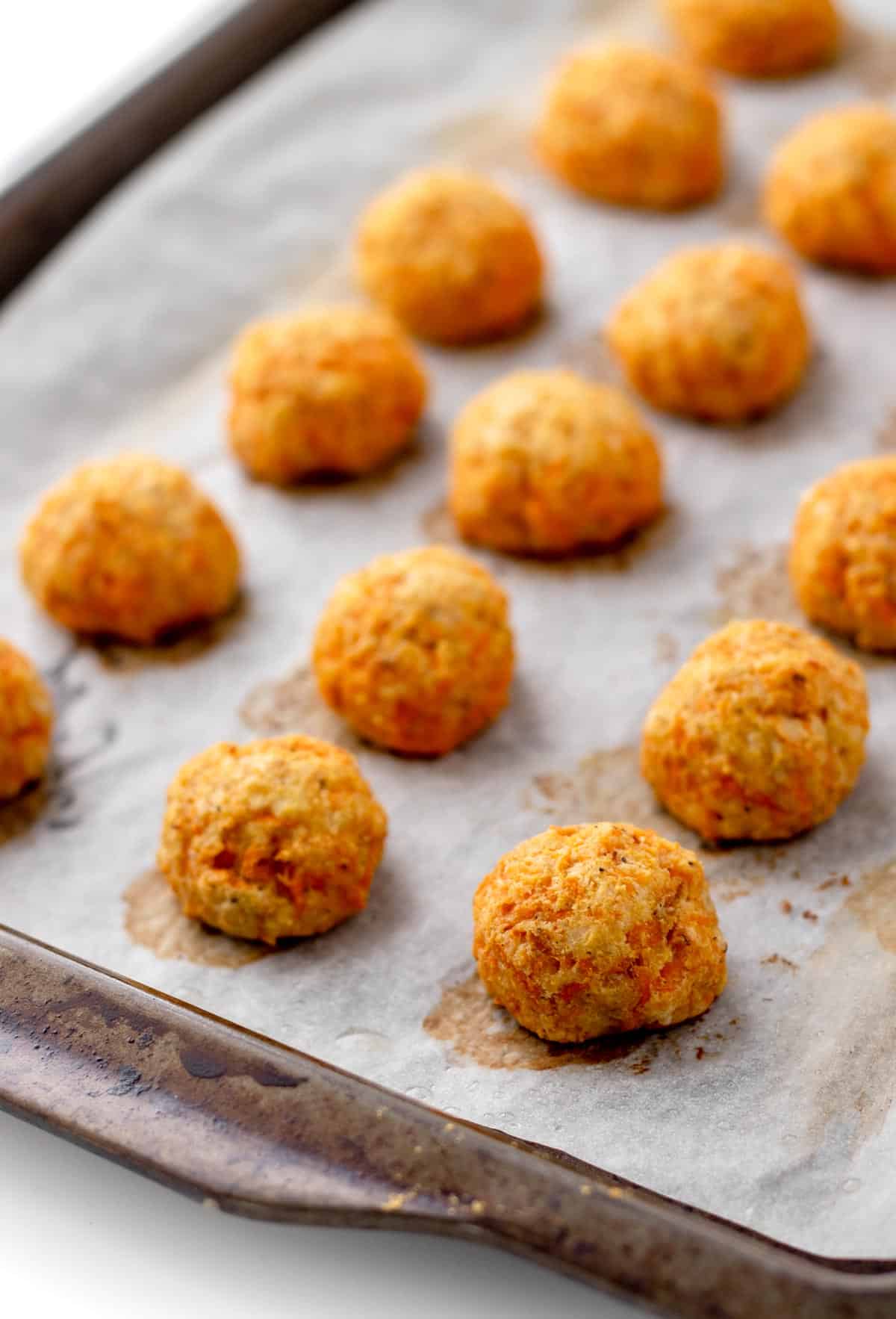 Healthy cheesy carrot balls on a baking sheet lined with parchment paper.