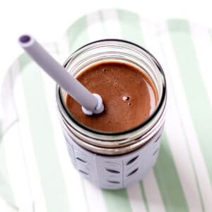 A chocolate black bean smoothie in a cup with a purple straw.