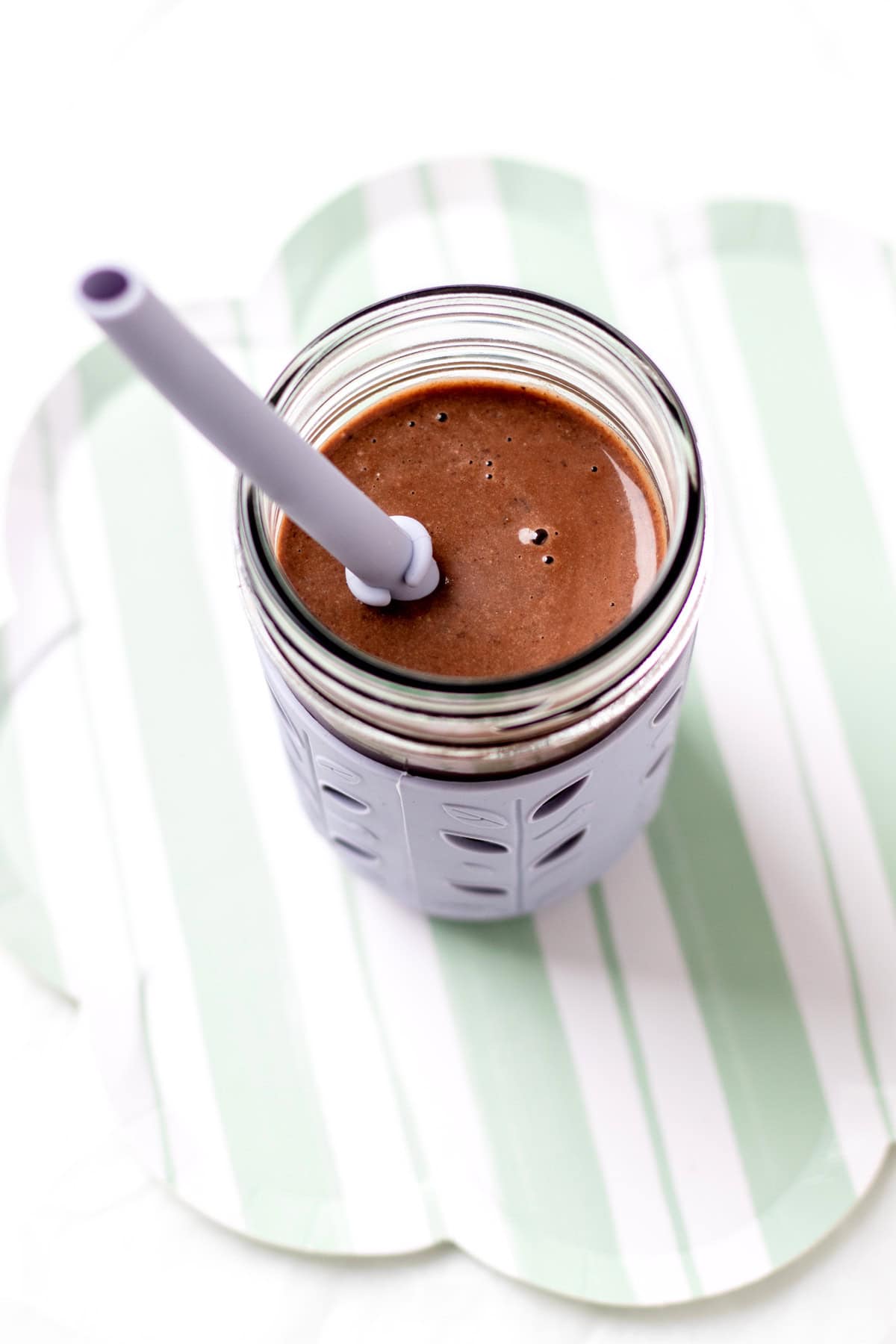 A creamy chocolate black bean smoothie in a cup with a straw on a decorative green plate.