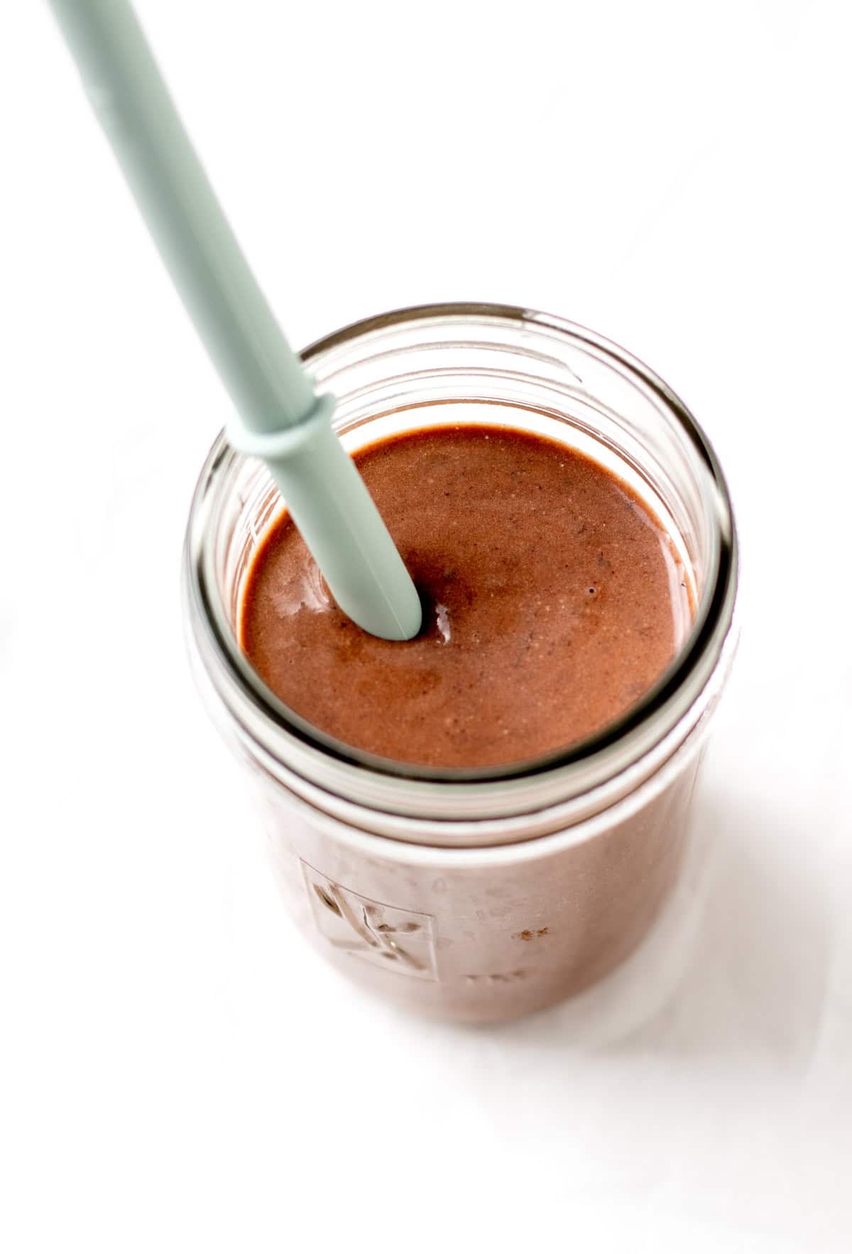 A chocolate black bean smoothie in a glass cup with a straw in it.