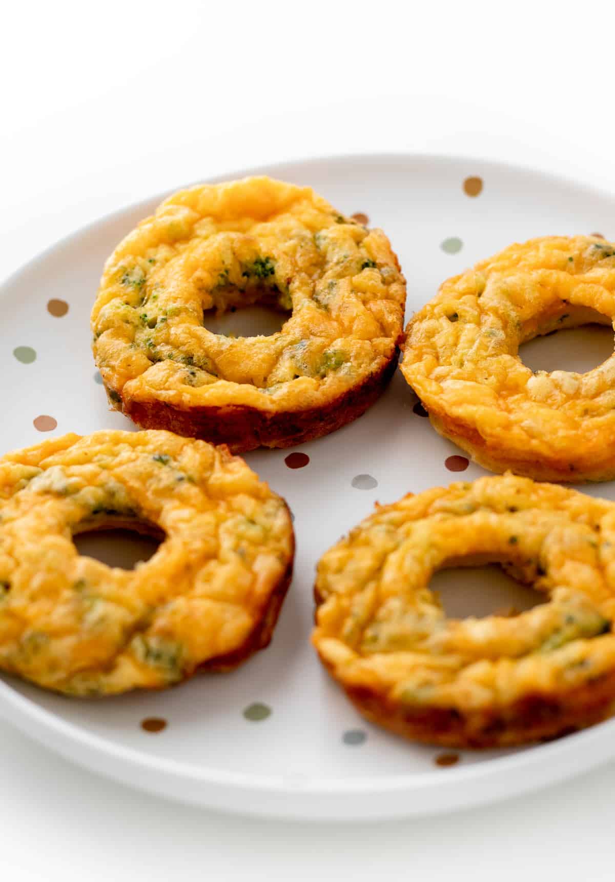 4 broccoli and cheese egg donuts on a colorful polka dotted plate.