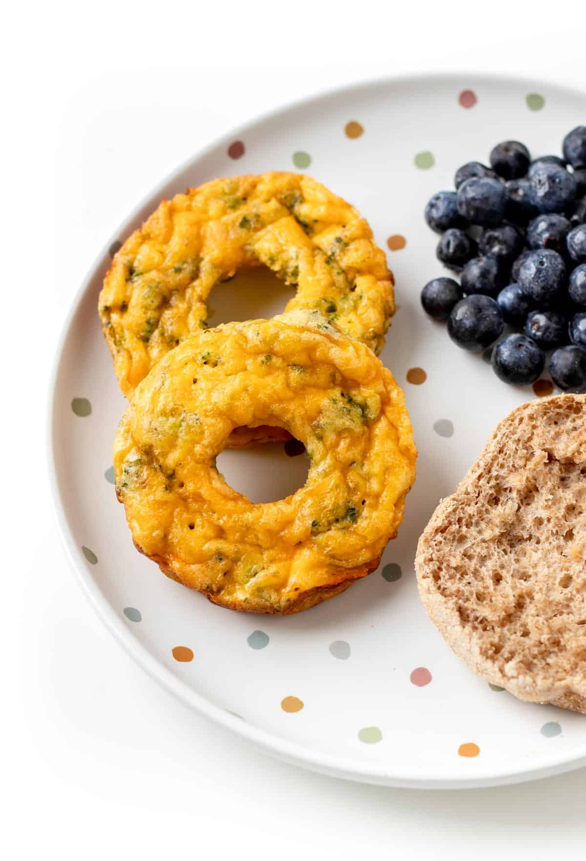 Two egg donuts on a polka dot plate with a half of an English muffin and blueberries.