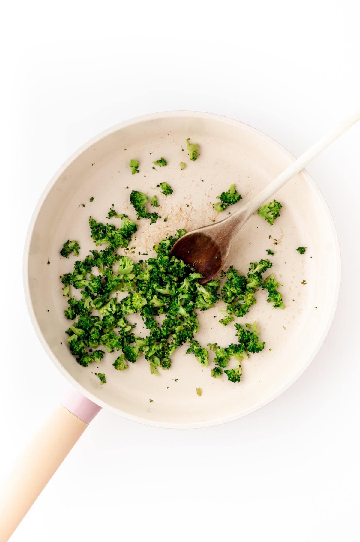 Broccoli simmering in a small skillet with a wooden spoon.