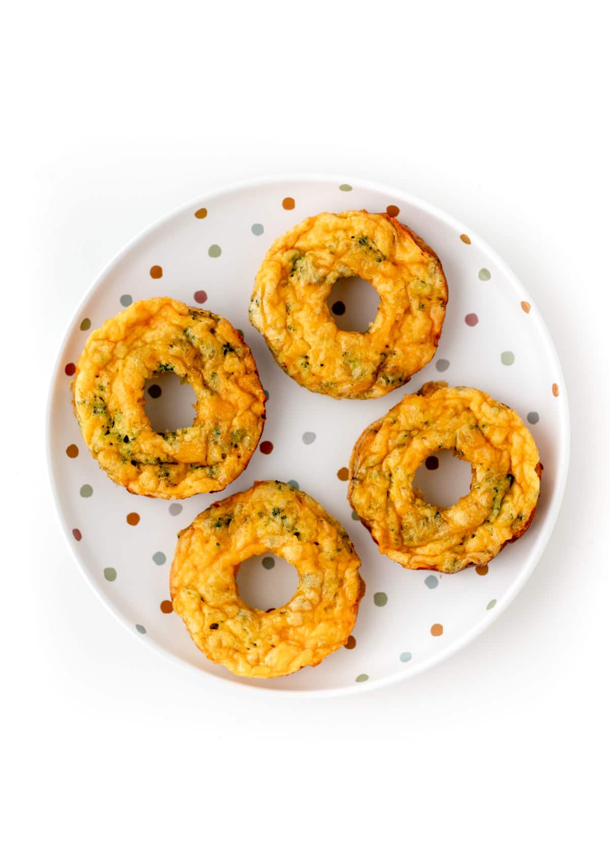 A birds-eye view of four broccoli and cheese healthy egg donuts on a polka dotted plate.