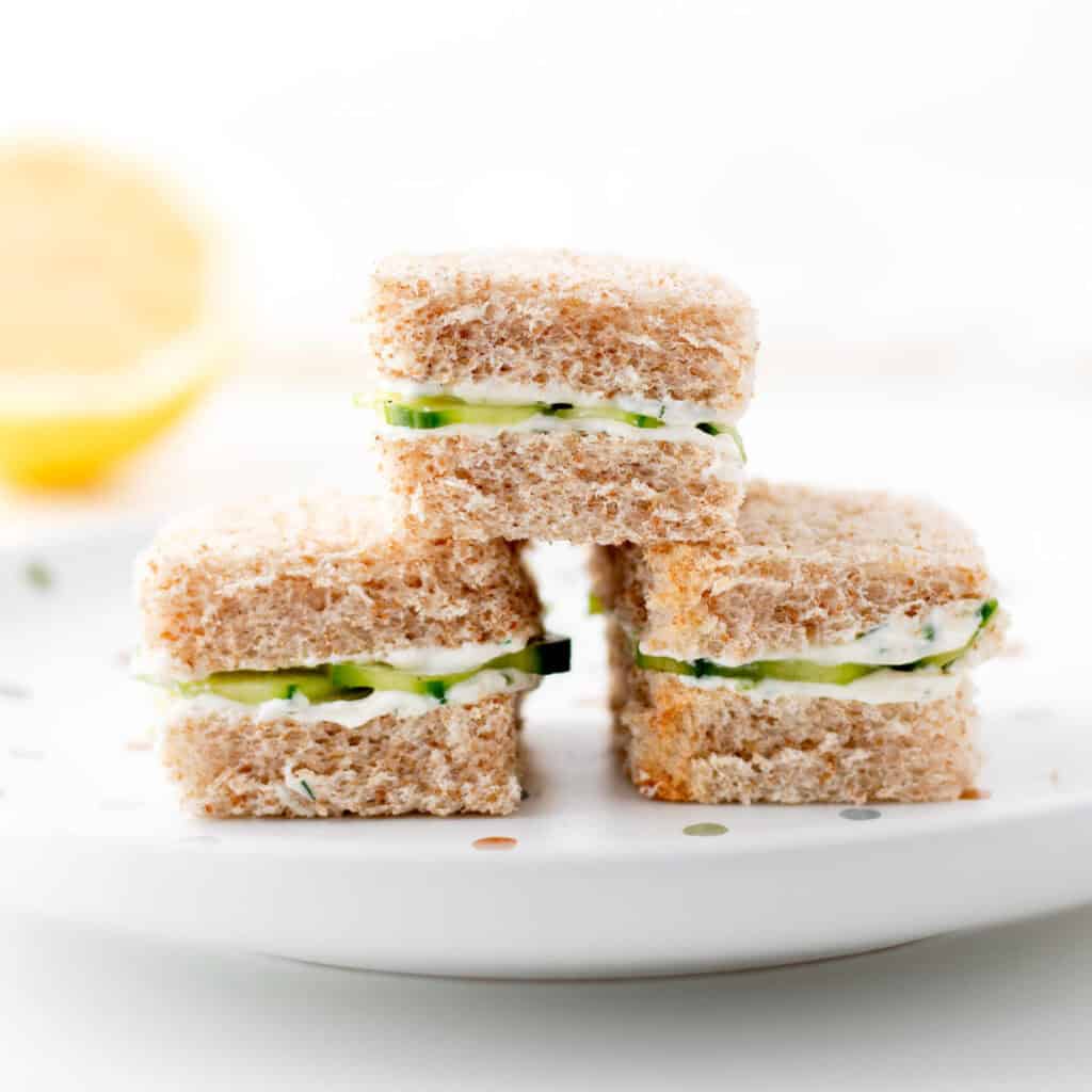 Mini cucumber sandwiches with herbed cream cheese on a plate.