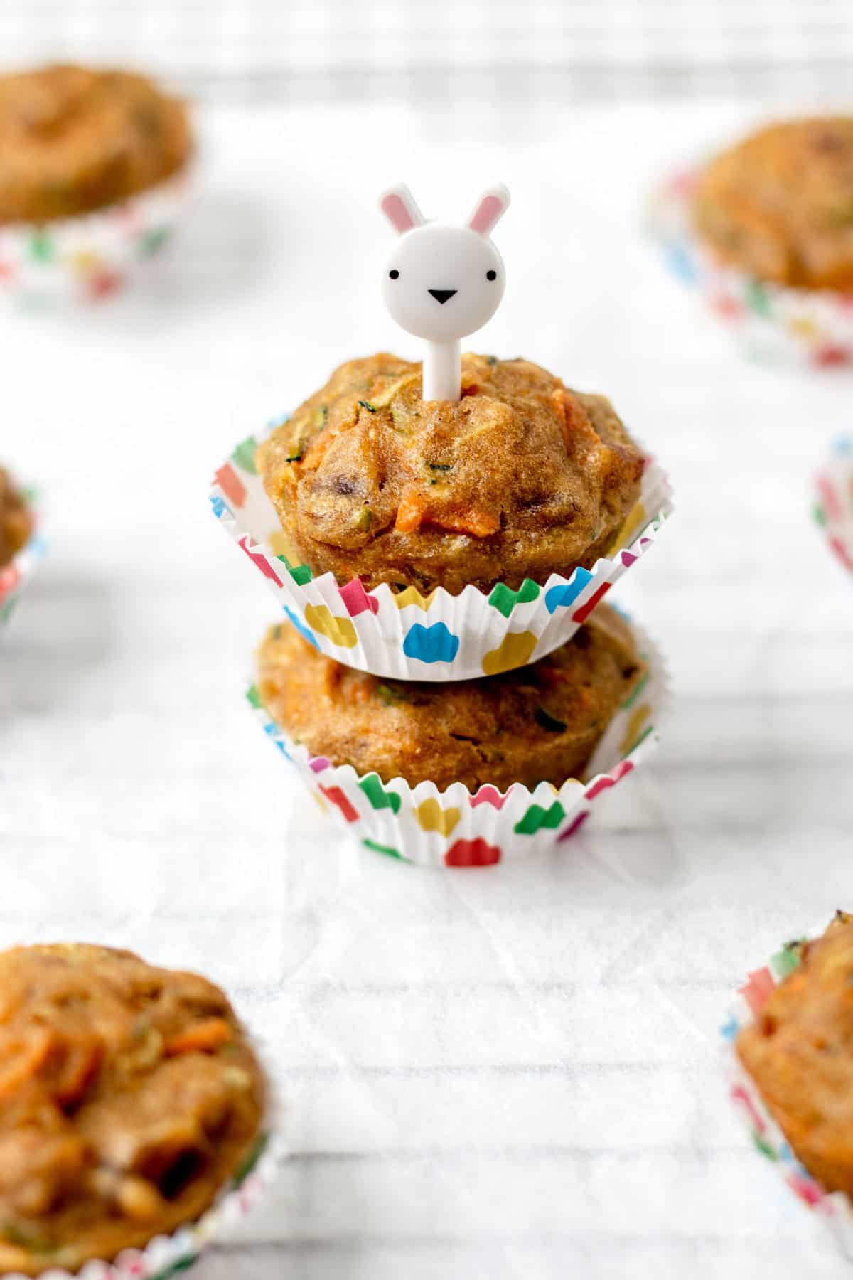 Two carrot zucchini banana muffins on top of one another with a toothpick in the top.