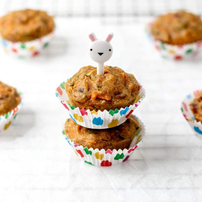 Two stacked carrot zucchini banana muffins with a bunny pick poked in the top.