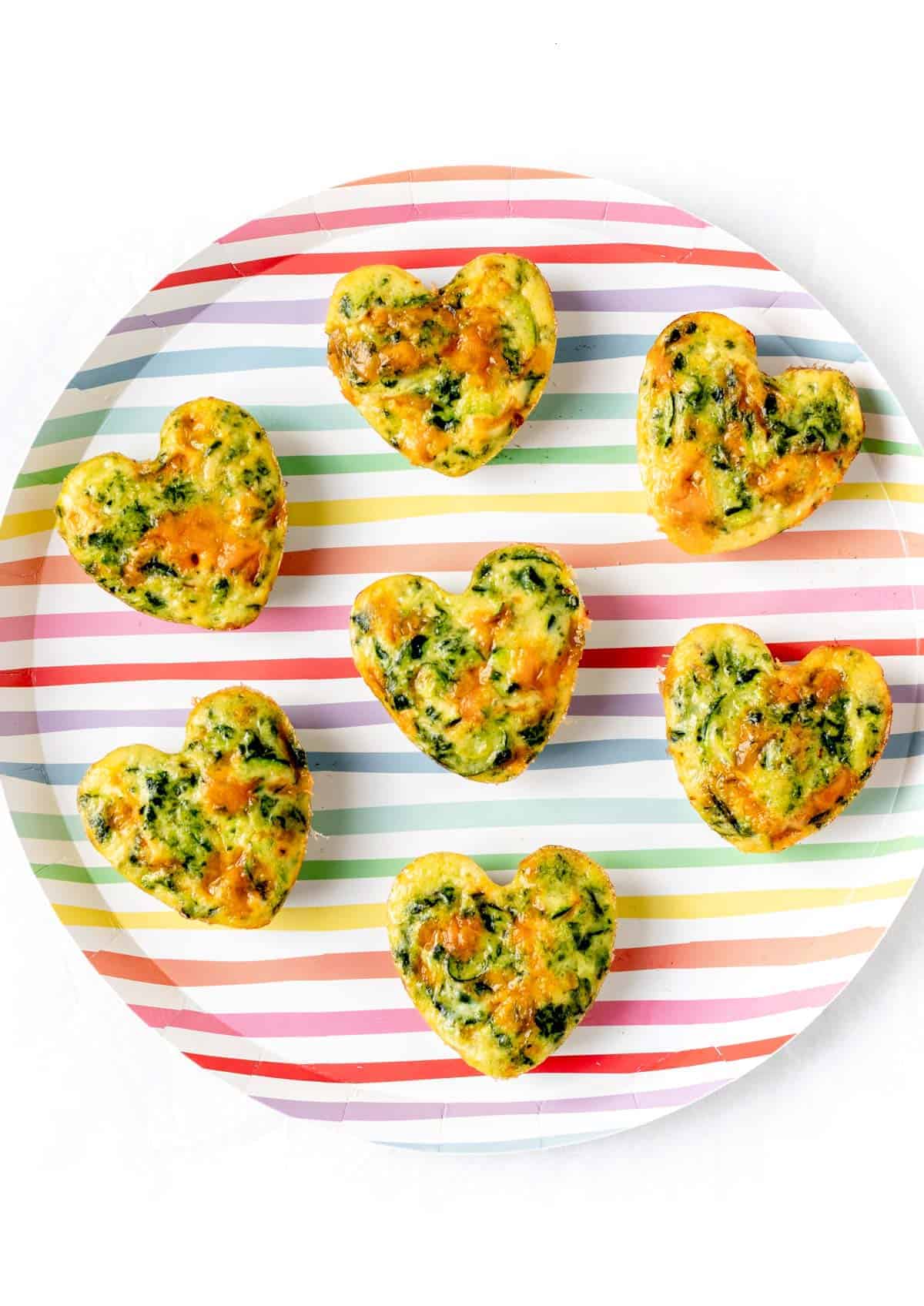 Heart shaped zucchini frittata muffins on a colorful striped plate.