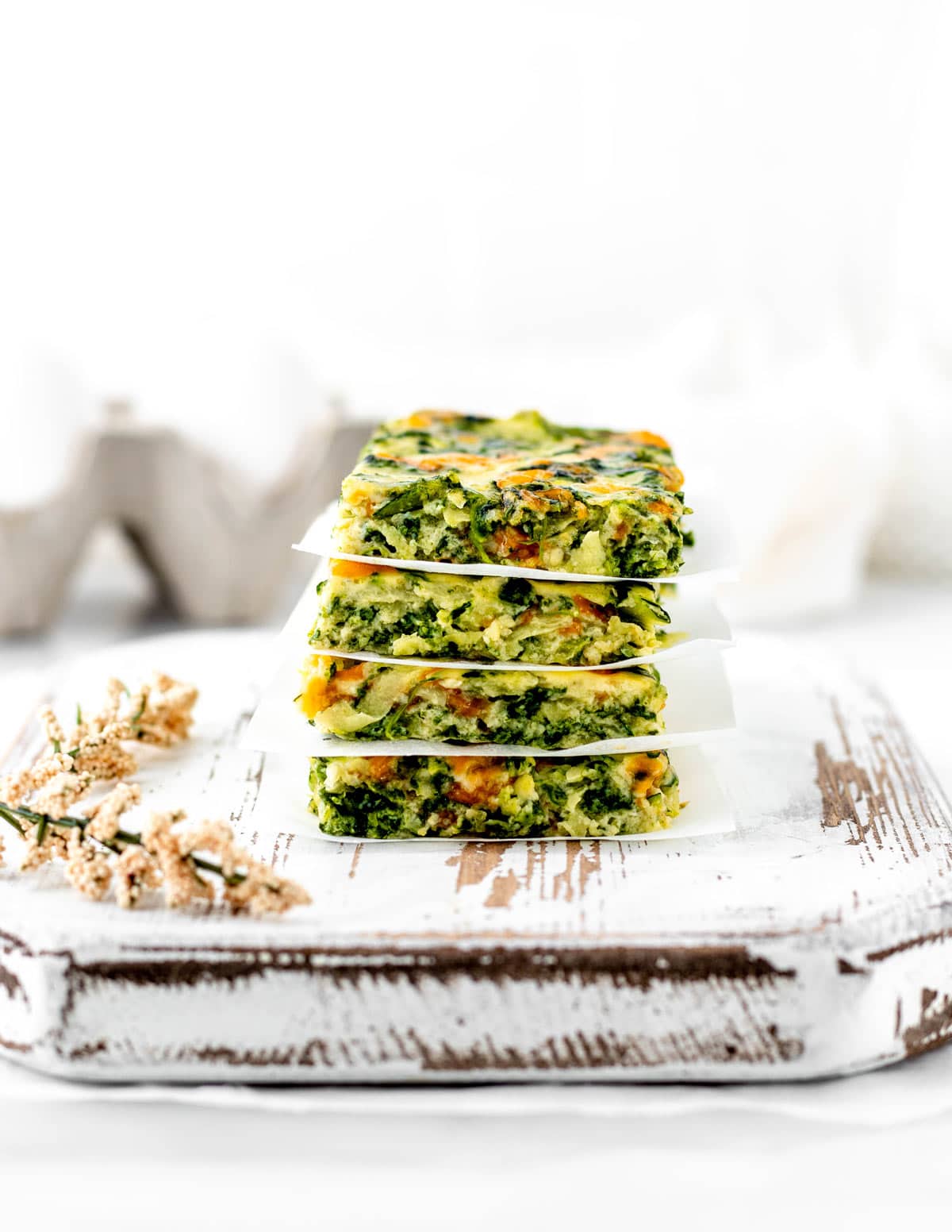 Baby frittata fingers stacked on top of one another on a decorative cutting board.