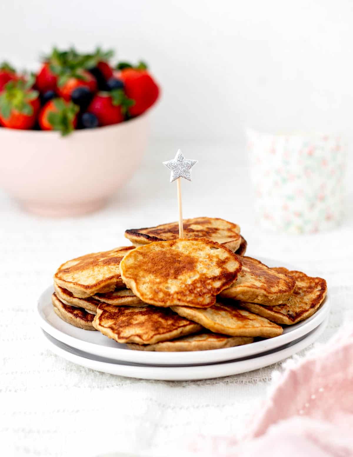 Baby cereal pancakes on a stack of two white plates on a table.