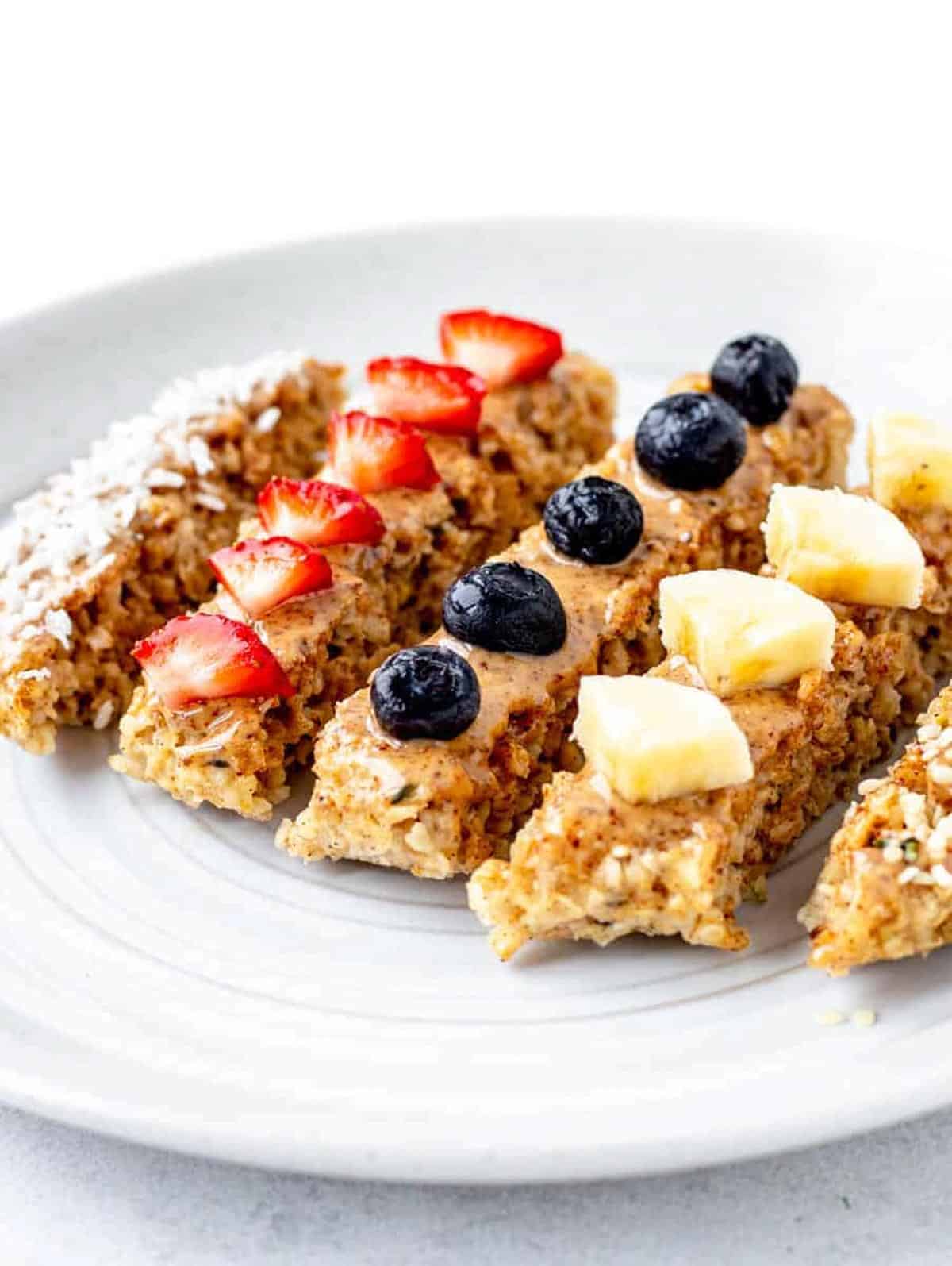 Baby oatmeal fingers topped with various fruits on a white plate.