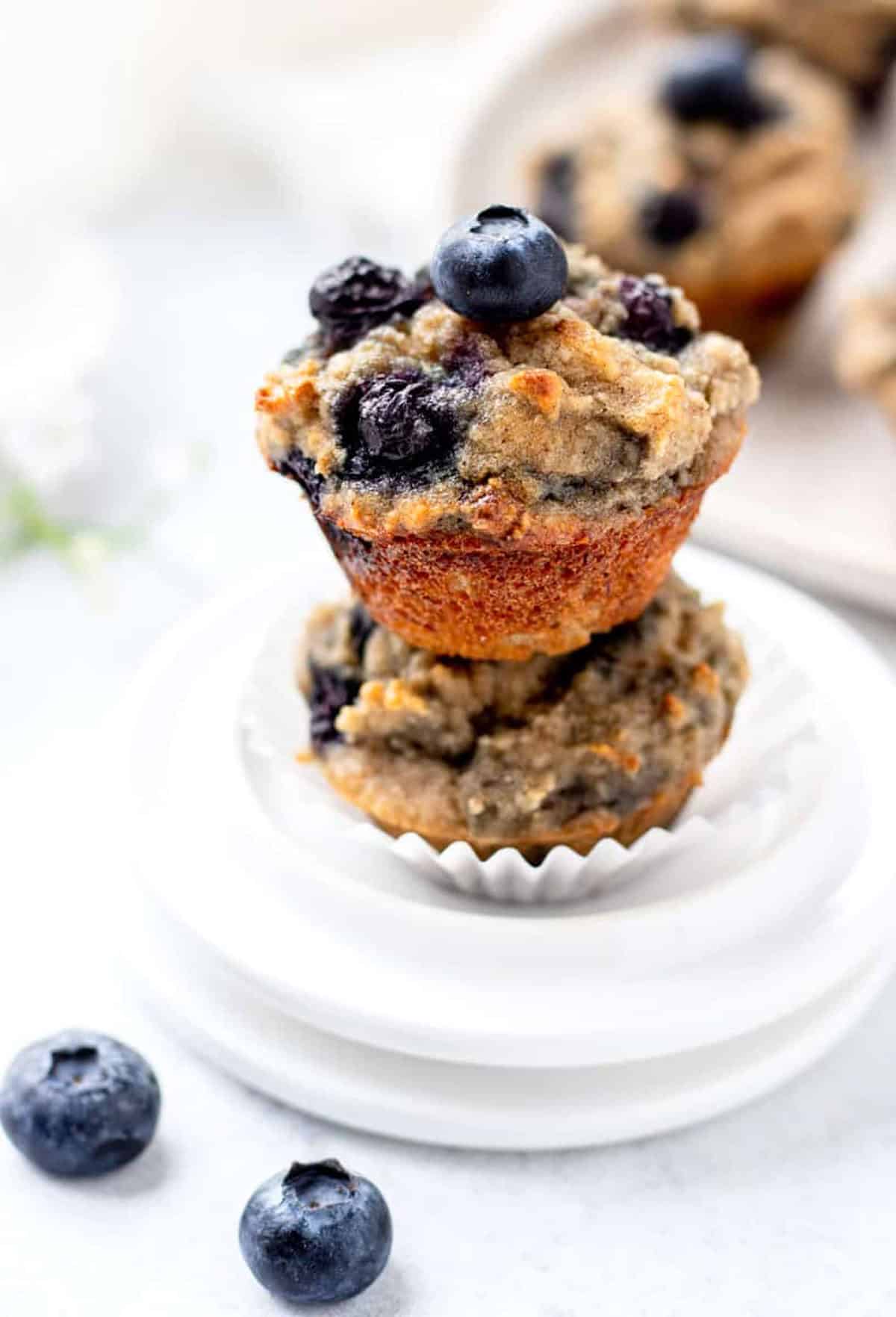 Two mini blueberry muffins stacked on top of one another on a small white plate.