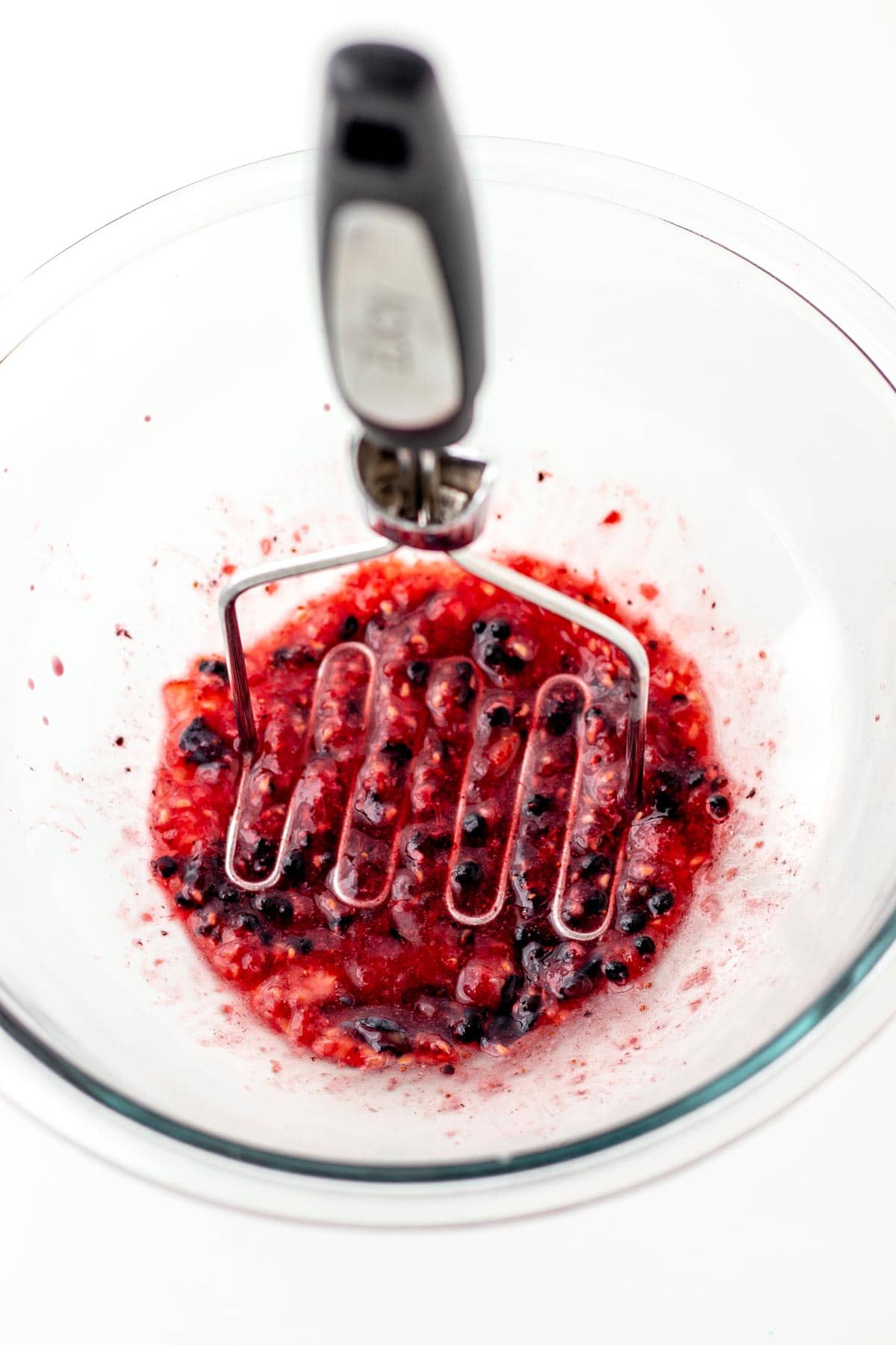 Mashing the berries in a bowl with a potato masher.