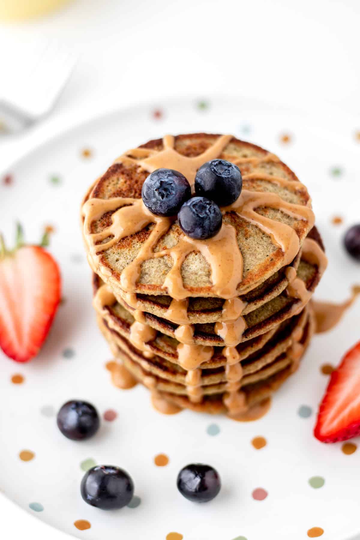 A stack of banana zucchini pancakes topped with blueberries and peanut butter.