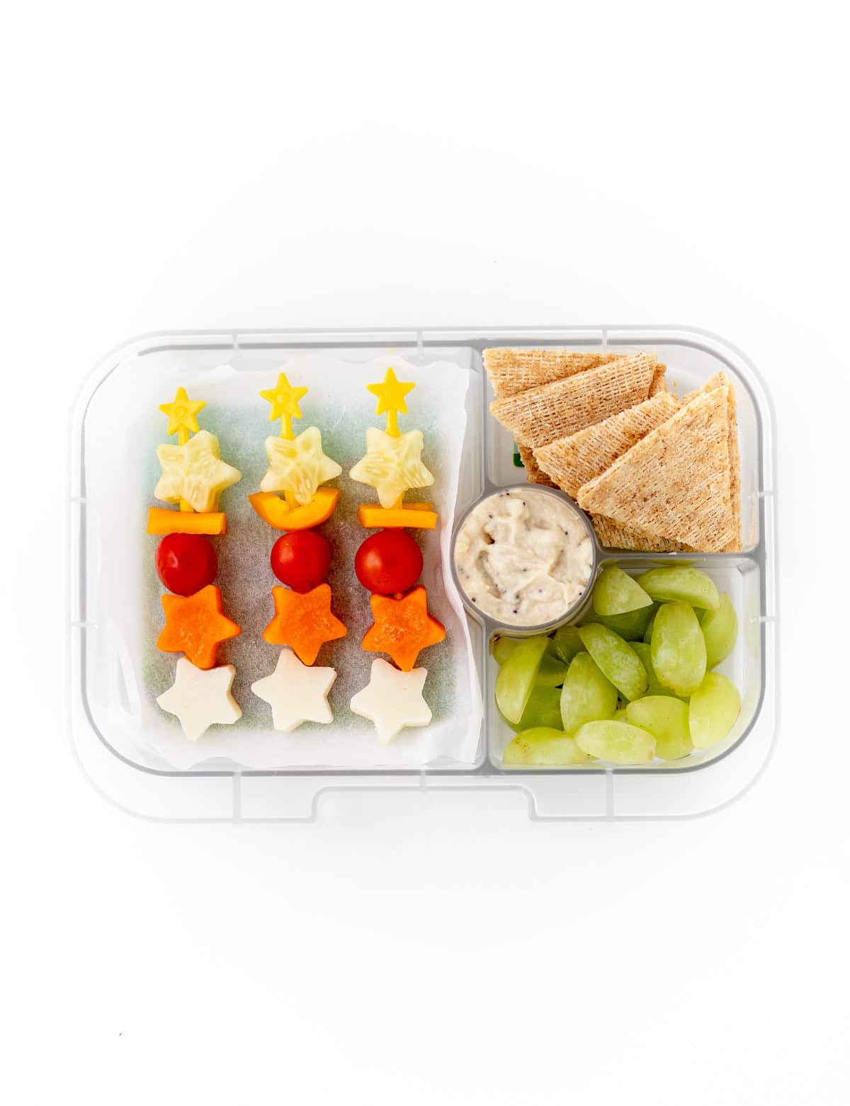 A lunchbox with raw veggie kabobs cut into star shapes along with pita wedges, hummus and grapes.