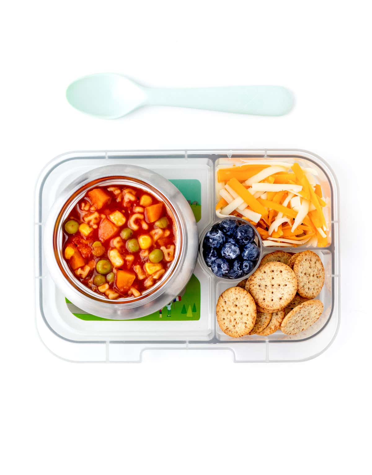 A lunchbox with a bowl of soup in it along with fruits, veggies and crackers.