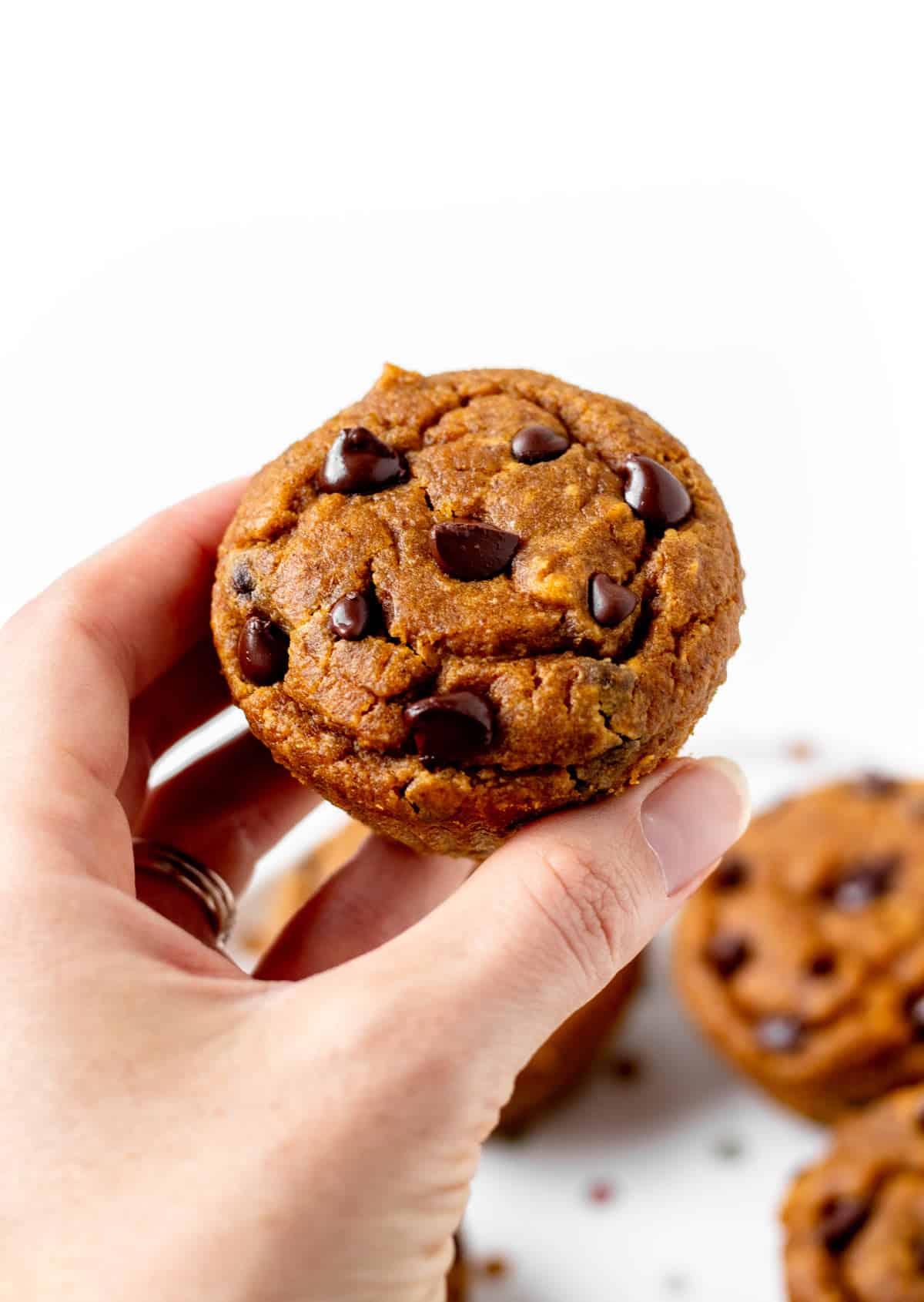 A hand holding up a pumpkin peanut butter muffin with a bite taken out of it.