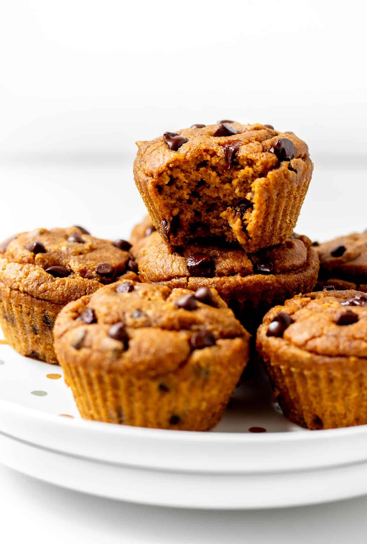 A half bitten pumpkin peanut butter muffin on top of more muffins on a plate.