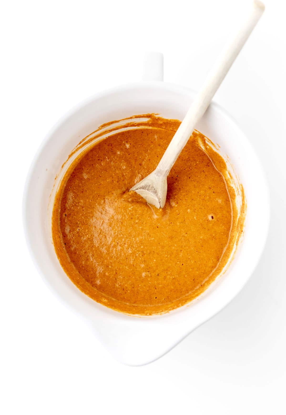 Combining the wet and dry ingredients for the pumpkin muffins in a white bowl with a spoon.